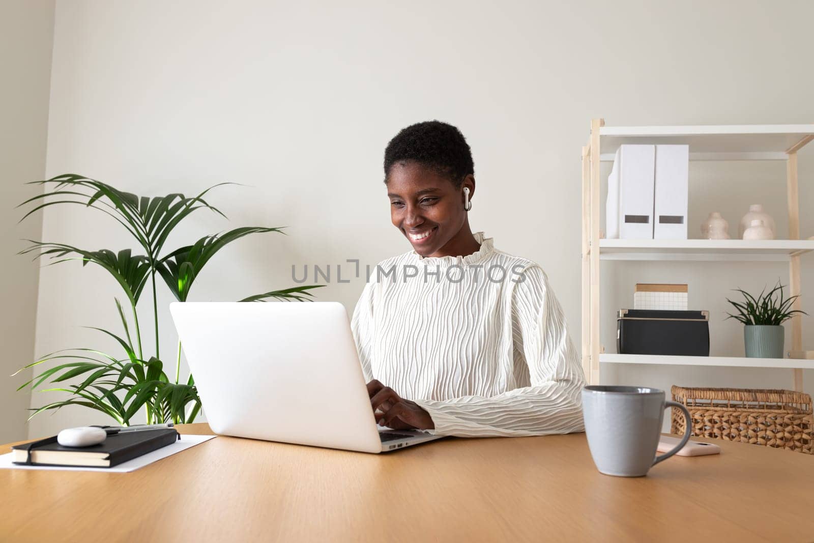 Black female entrepreneur working at home office. Happy African American woman using laptop and wireless earphones. Working from home concept.