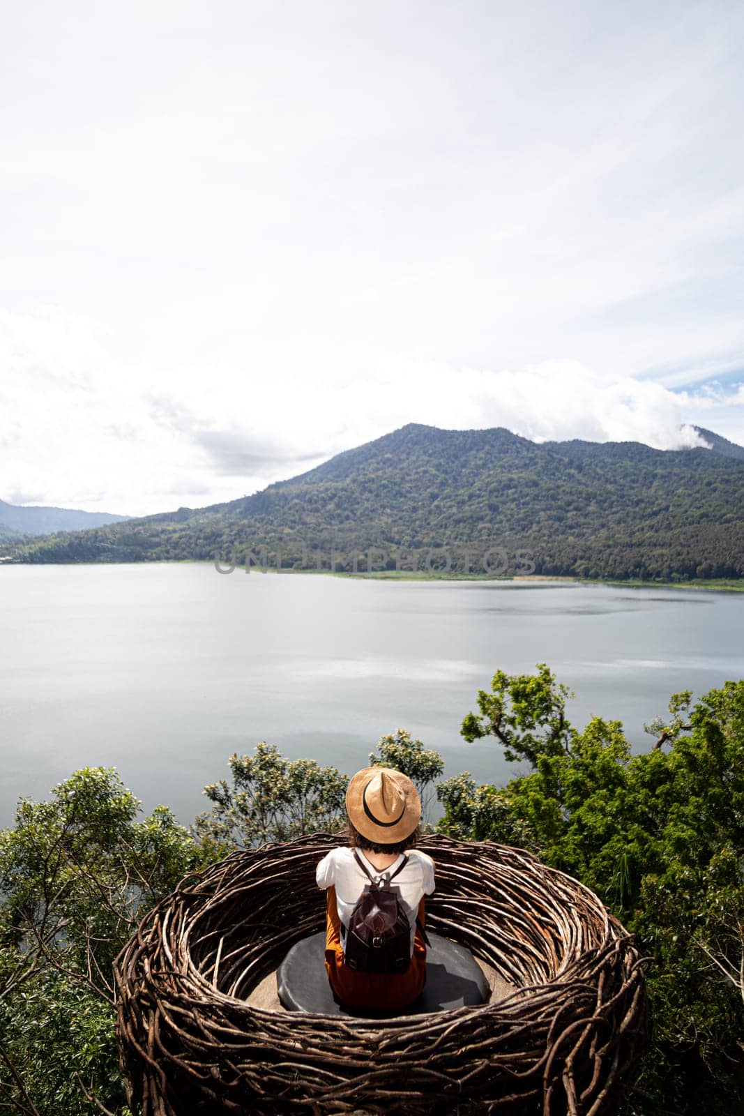 Tourist woman contemplating nature sitting in straw nest looking at lake view and mountains in Bali. Copy space.Vertical by Hoverstock