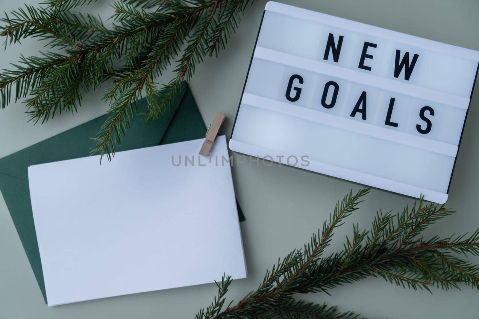 Lightbox with inspirational message NEW GOALS with fir branches on pastel background. Happy new year promises resolutions concept. Copy space envelope Christmas mockup for lettering art drawing sample Self growth and personal development