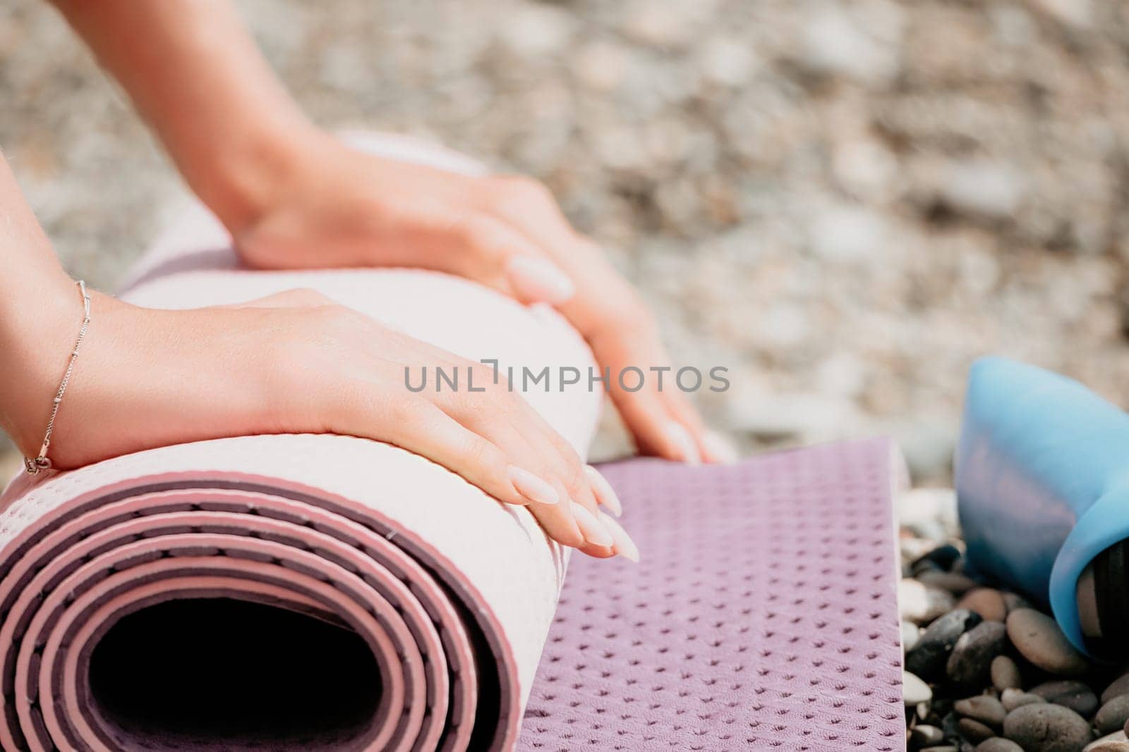 Young woman with long hair in white swimsuit and boho style braclets practicing outdoors on yoga mat by the sea on a sunset. Women's yoga fitness routine. Healthy lifestyle, harmony and meditation