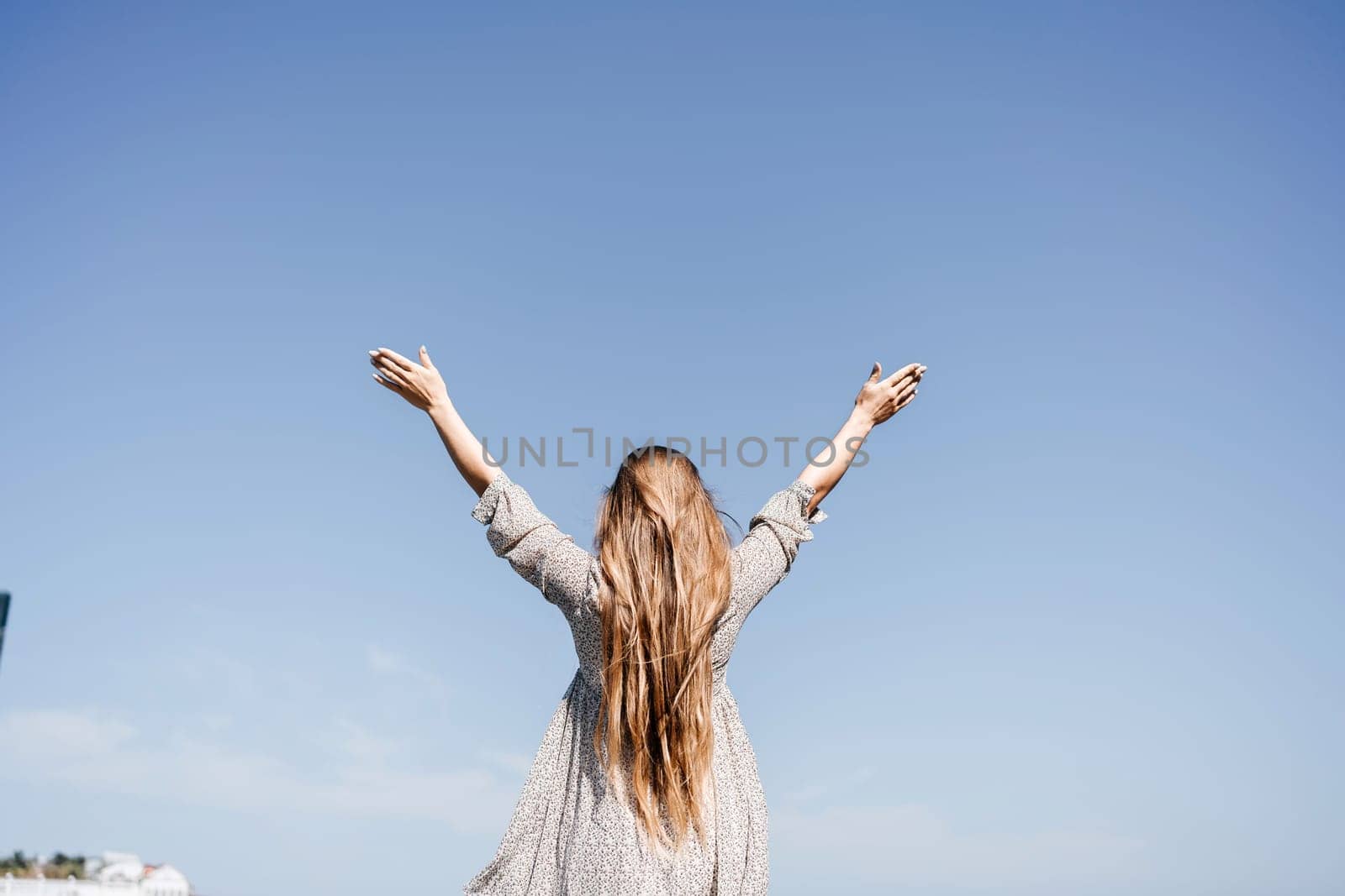 A woman with long hair is standing on the beach, looking up at the sky. She is wearing a dress and she is happy