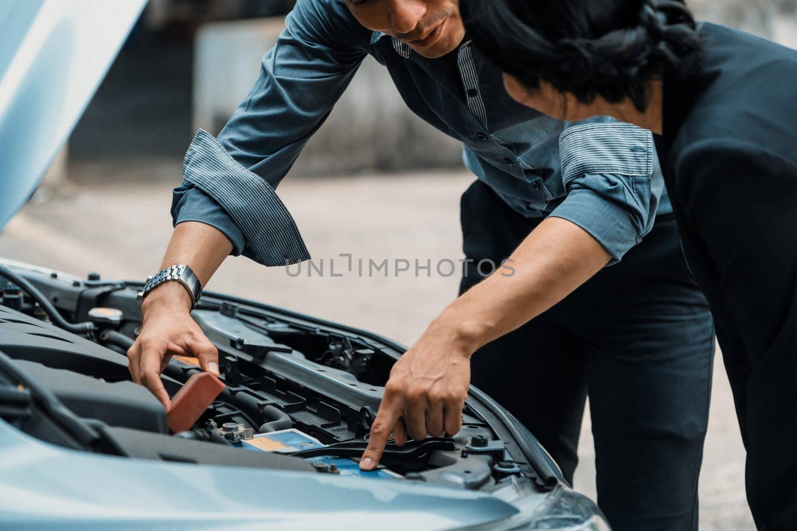 Man help woman fix the car problem. He pop up the car hood to repair the damaged part. uds