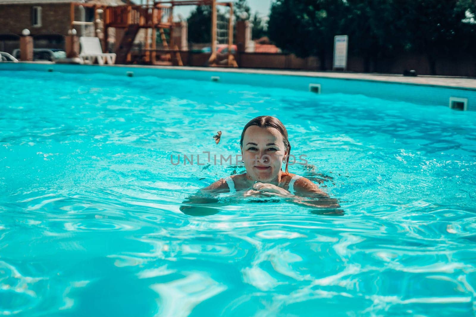 A woman is swimming in a pool. She is smiling and looking at the camera. The pool is blue and the water is calm