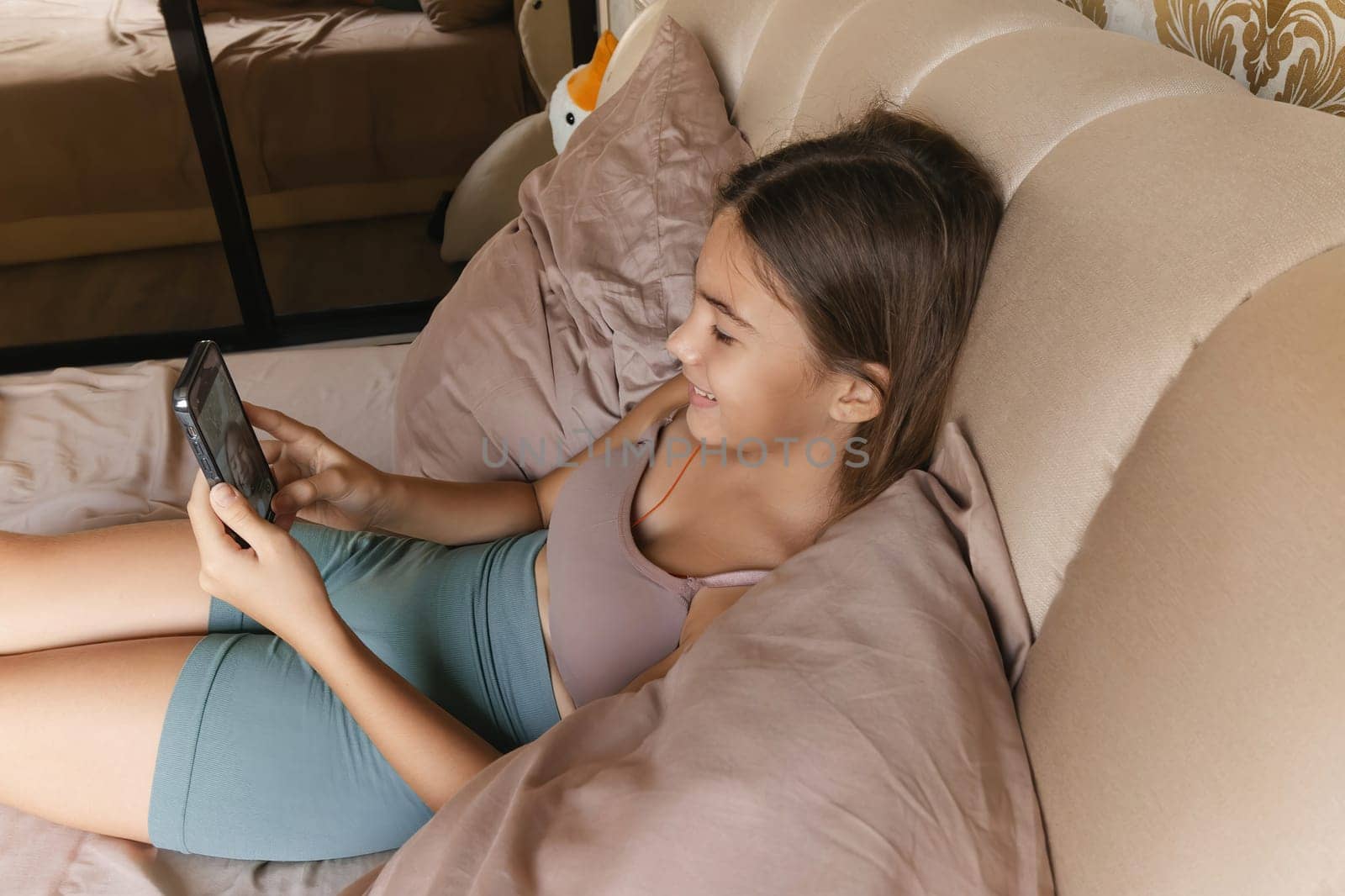 A girl is laying on a bed with a cell phone in her hand. She is smiling and she is enjoying herself