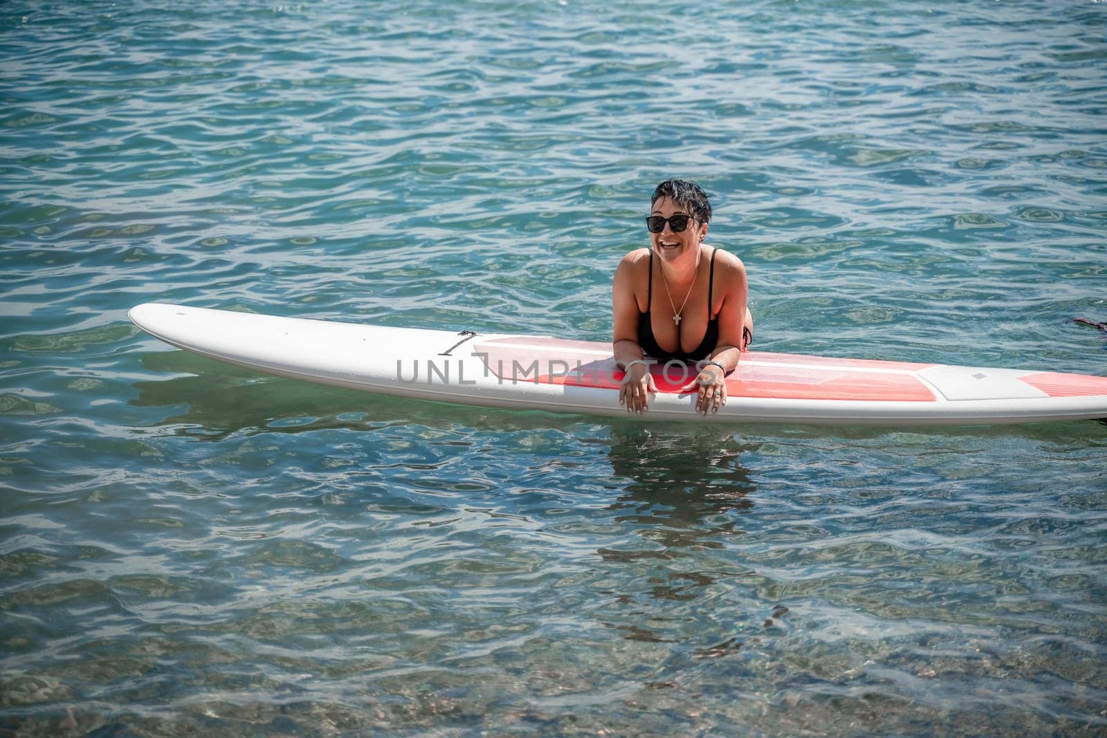 Woman sap sea. Sports girl on a surfboard in the sea on a sunny summer day. In a black bathing suit, he lies on a sap in the sea. Rest on the sea