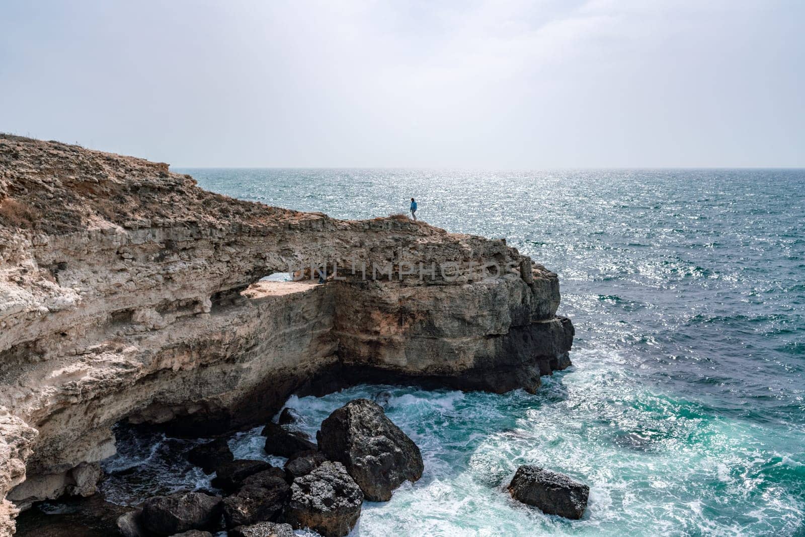 A rocky cliff overlooks the ocean, with the water crashing against the rocks. The scene is serene and peaceful, with the sound of the waves providing a calming atmosphere