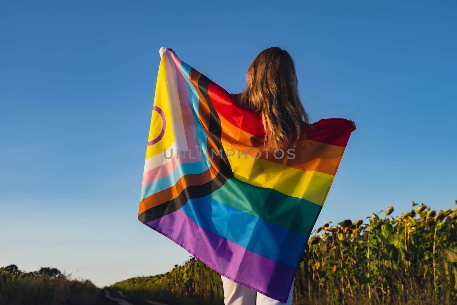 Girl showing her gender identity. Young woman stand with pride flag Rainbow LGBTQIA flag made from silk material on field background. Symbol of LGBTQ pride month. Equal rights. Peace and freedom concept