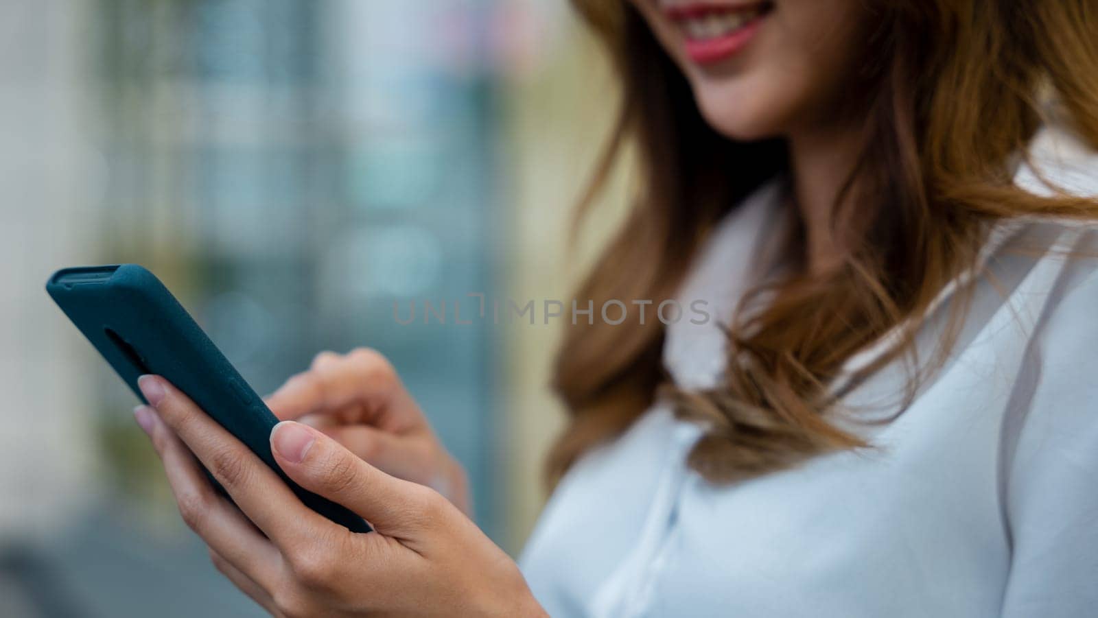 A woman in a white shirt typing a message on her smartphone. The device is an essential tool for modern communication and digital lifestyle, offering connectivity and convenience.
