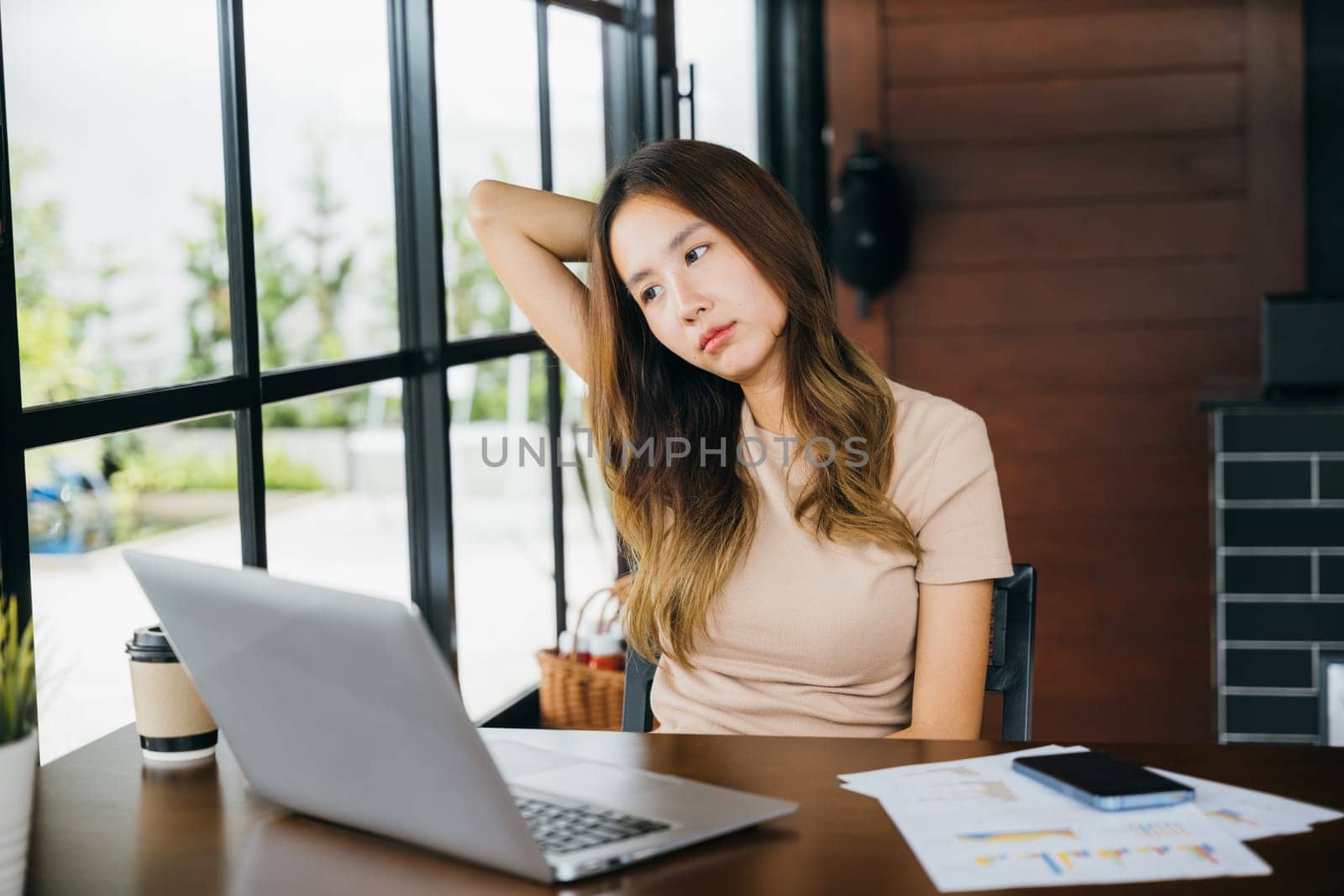 Tired office woman sitting at desk touching massaging stiff neck while holding her head in cafe by Sorapop