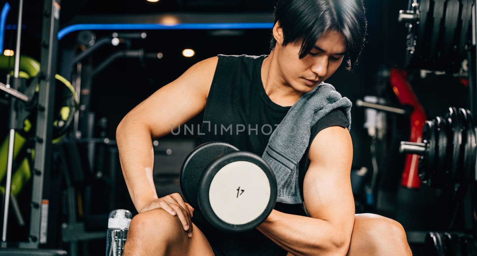 A fit and healthy young man sitting on a bench holding a dumbbell, working on his arm muscles and bicep, showcasing his dedication to maintaining a strong and muscular body. empty space