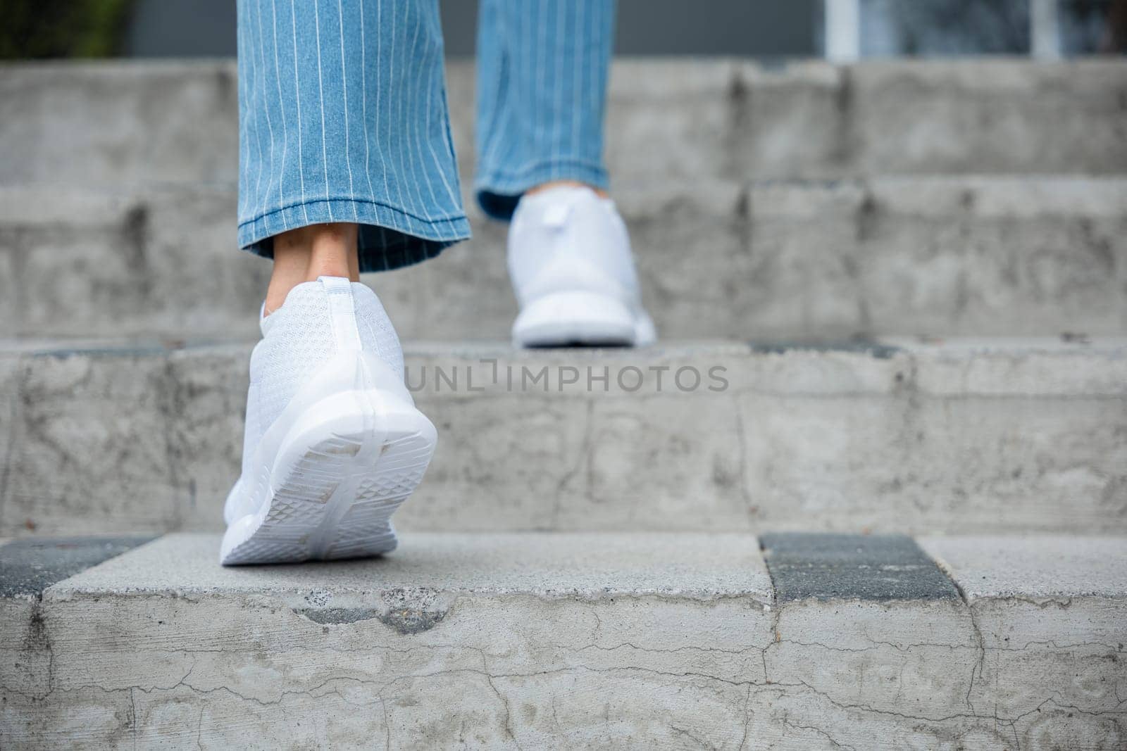 In the city, a businesswoman climbs the stairs in sneakers, signifying her commitment to success. Each step is a testament to her determination, progress, and professional growth. step up by Sorapop