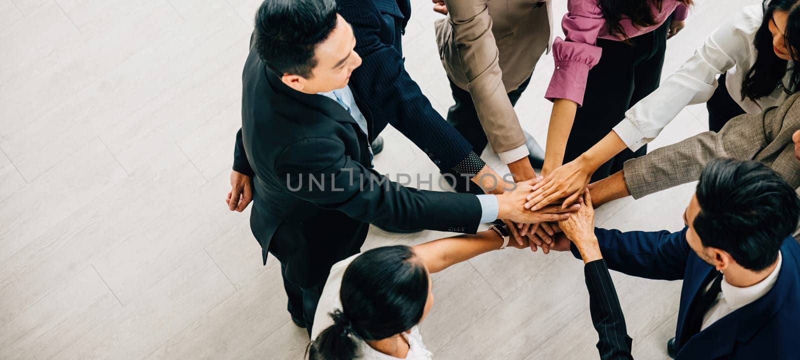 A top perspective reveals four diverse businesspeople standing in a circle stacking their hands. This image conveys the concepts of unity teamwork and global collaboration. by Sorapop