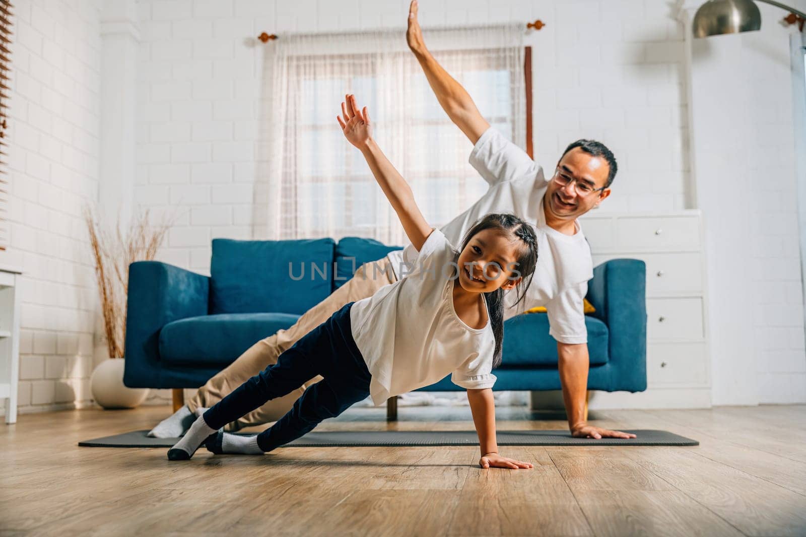 A father and his daughter find joy in yoga at home practicing togetherness happiness by Sorapop