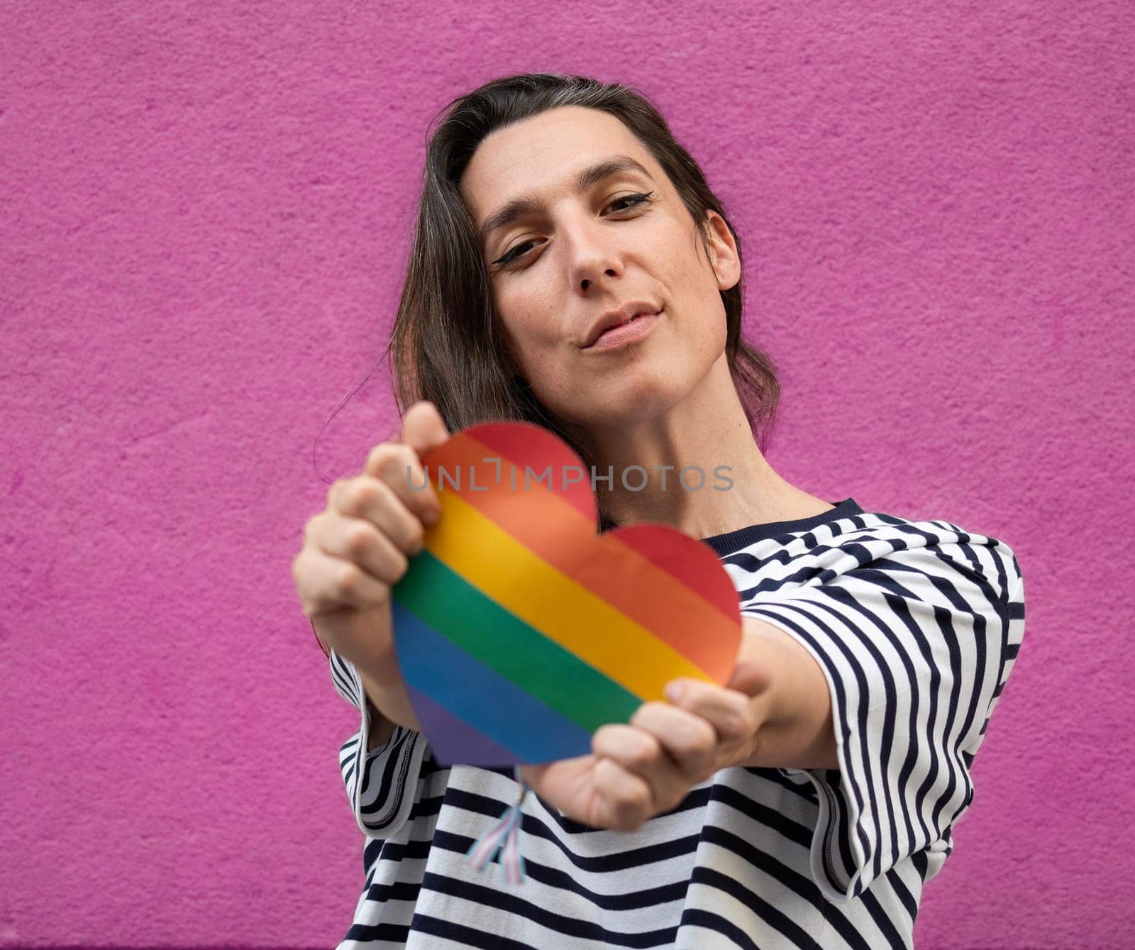 Close up front view of lesbian woman with a rainbow heart to support LGBT community isolated on pink background.
