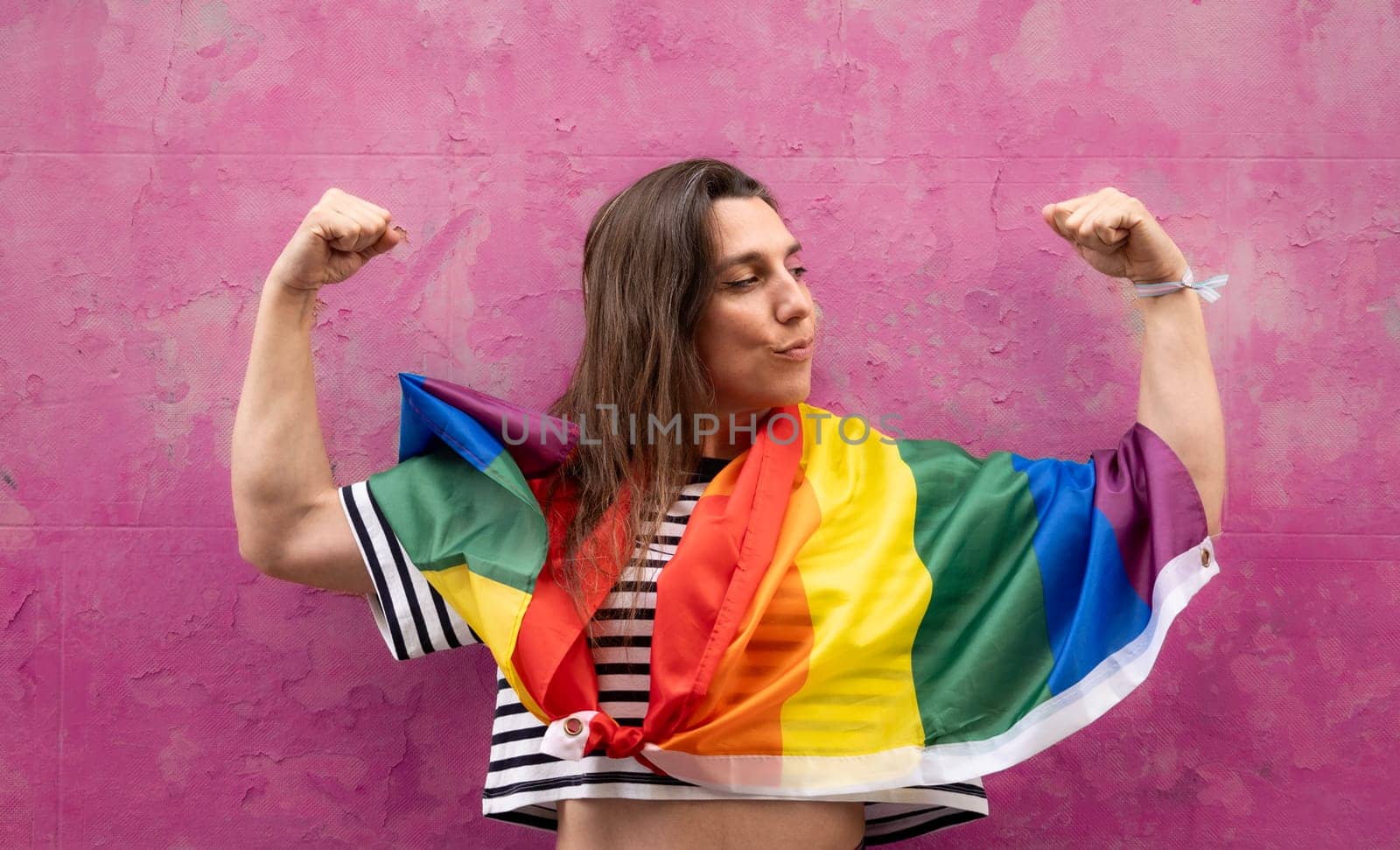 Lesbian woman in strong arm pose with rainbow flag isolated on pink background by papatonic