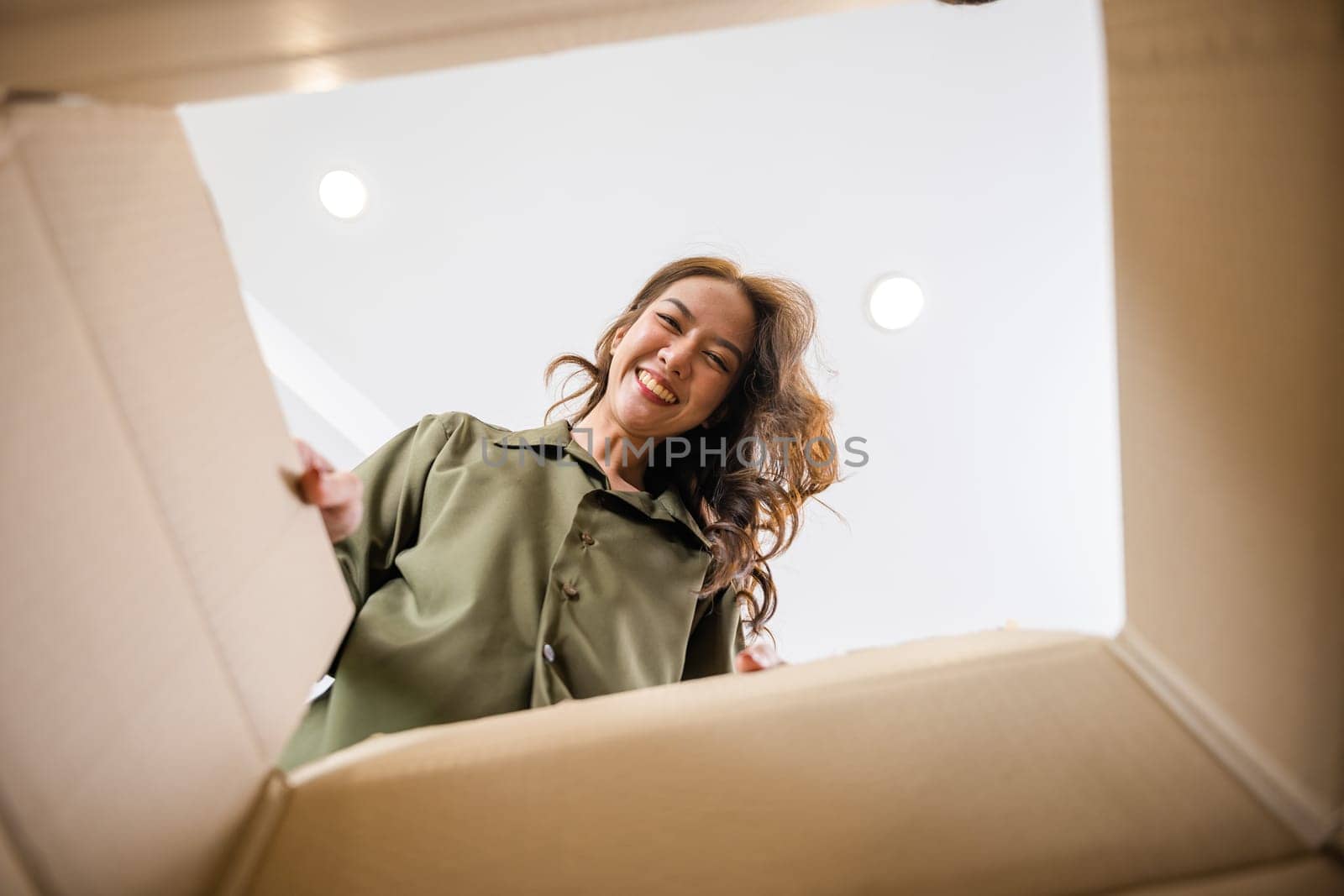 Happy Asian young woman opening carton box from internet store order shopping online at home, Smiling female surprised unpacking christmas gift big box and looking inside, inside bottom view