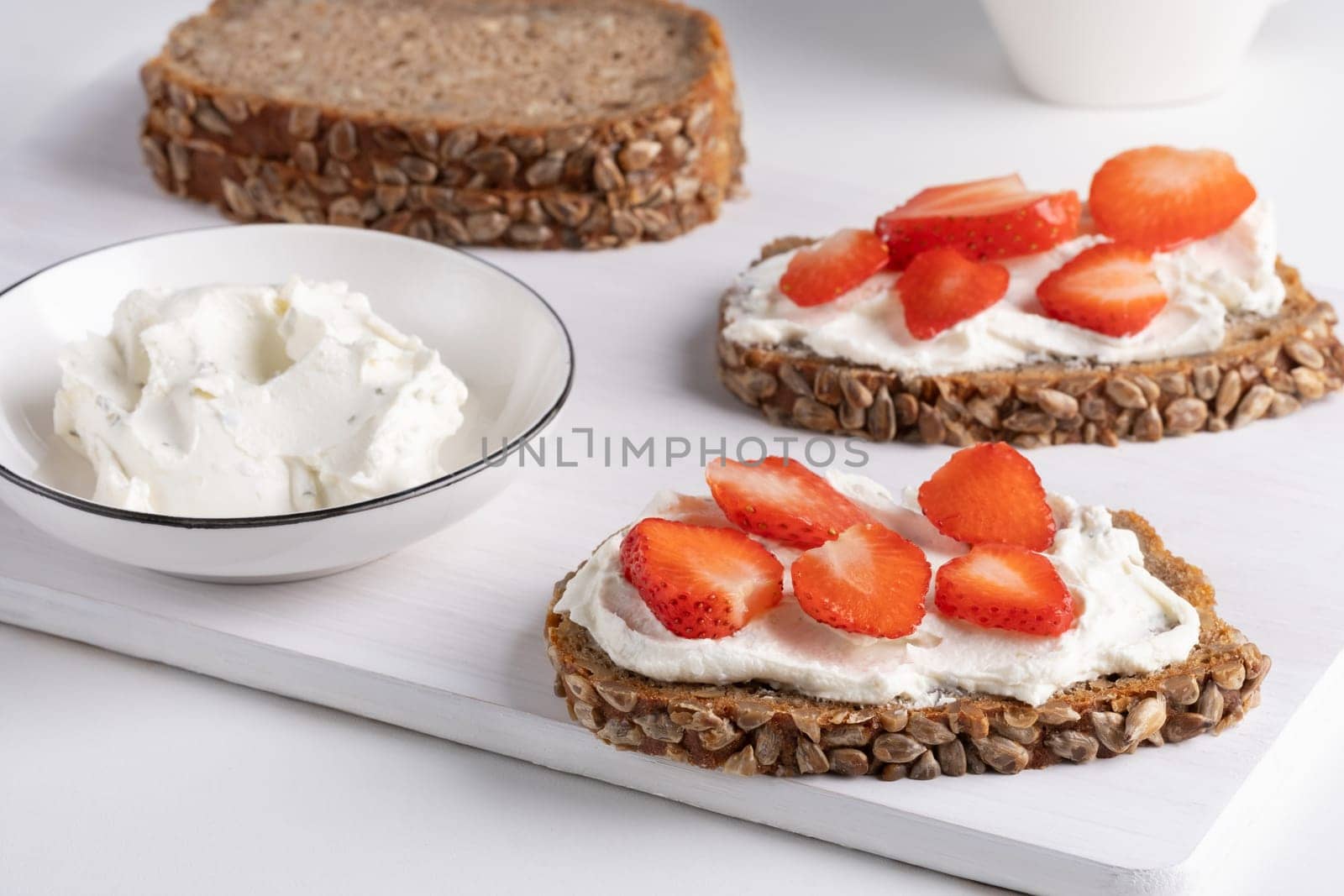 Rye bread with cream cheese and strawberry on a white table. Whole grain rye bread with seeds.