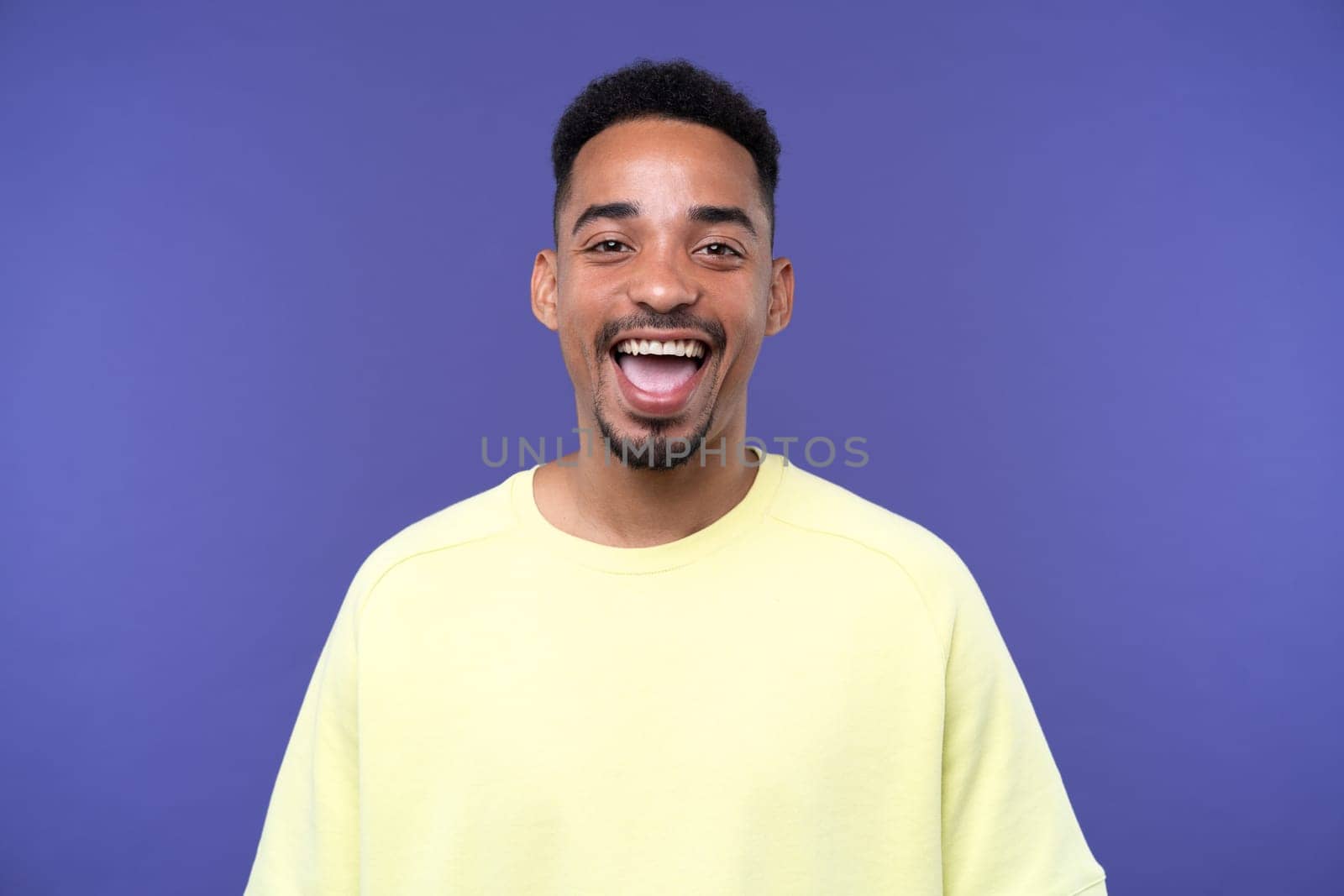 Emotional young black guy in casual raising fists up studio background, celebrating success, happy handsome african american millennial man sharing good emotions, copy space