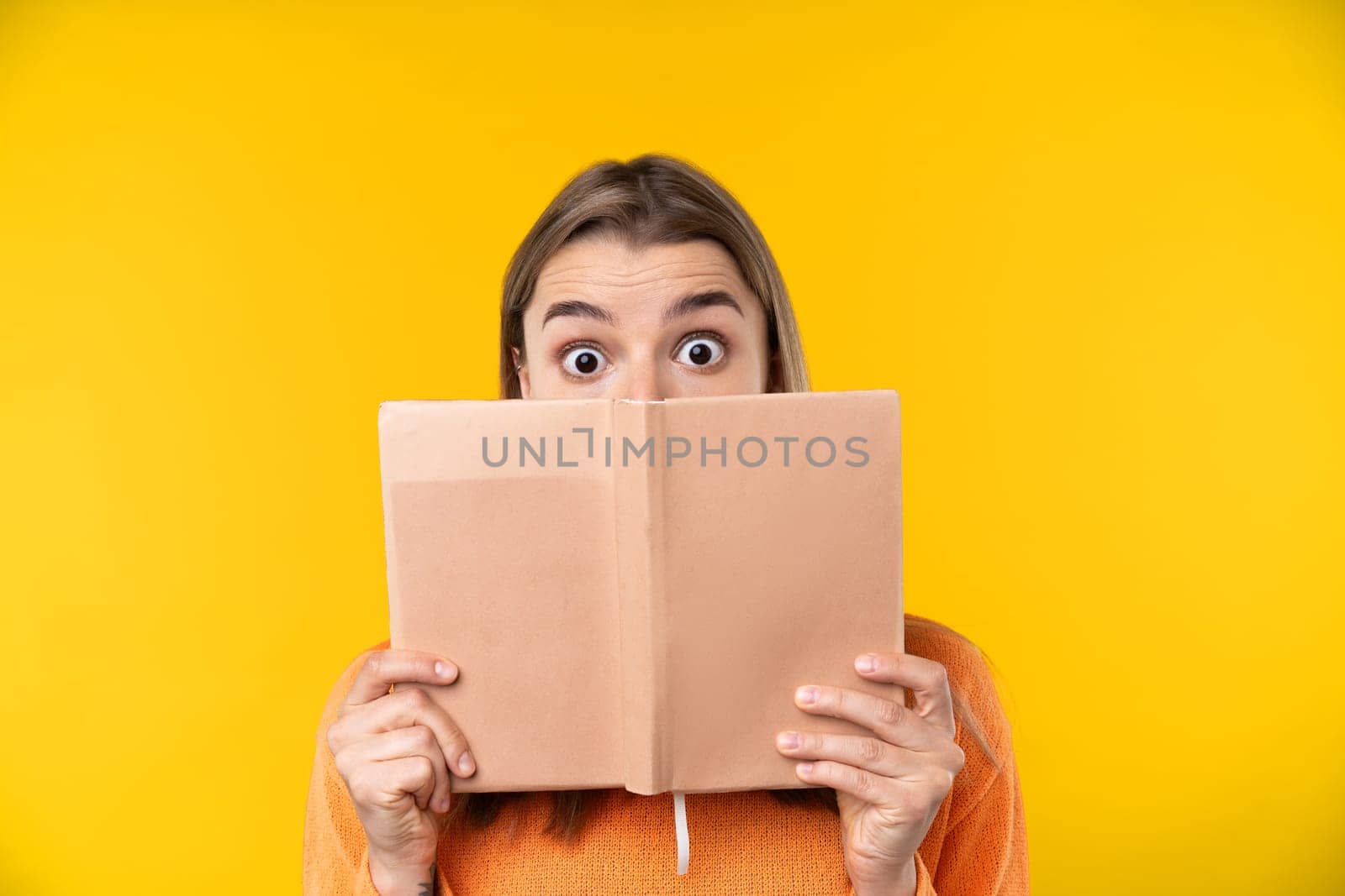 Happy emotions concept. Positive and beautiful young woman laughs poisitively looks aside with carefree face expression wears casual orange sweater isolated over yellow studio background.