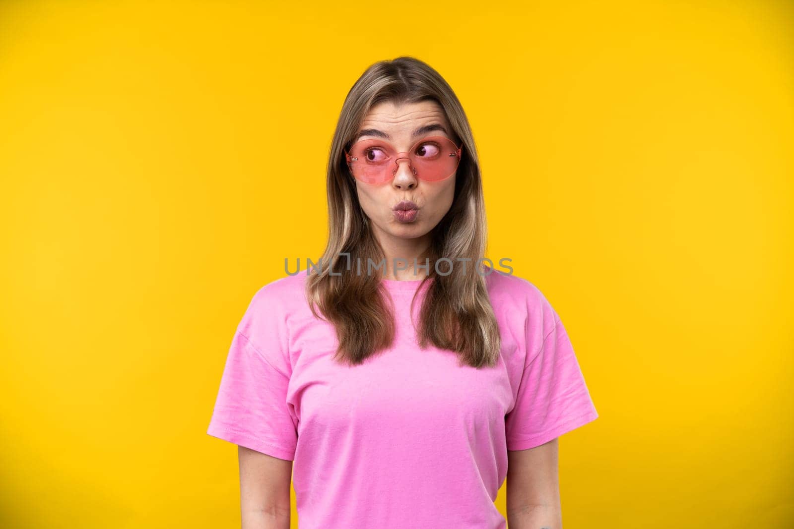 Happy emotions concept. Positive and beautiful young woman laughs poisitively looks aside with carefree face expression wears casual orange sweater isolated over yellow studio background.