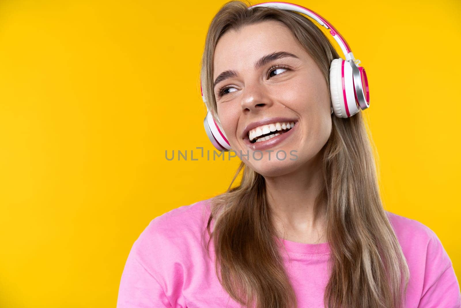 Happy emotions concept. Positive and beautiful young woman laughs poisitively looks aside with carefree face expression wears casual orange sweater isolated over yellow studio background.