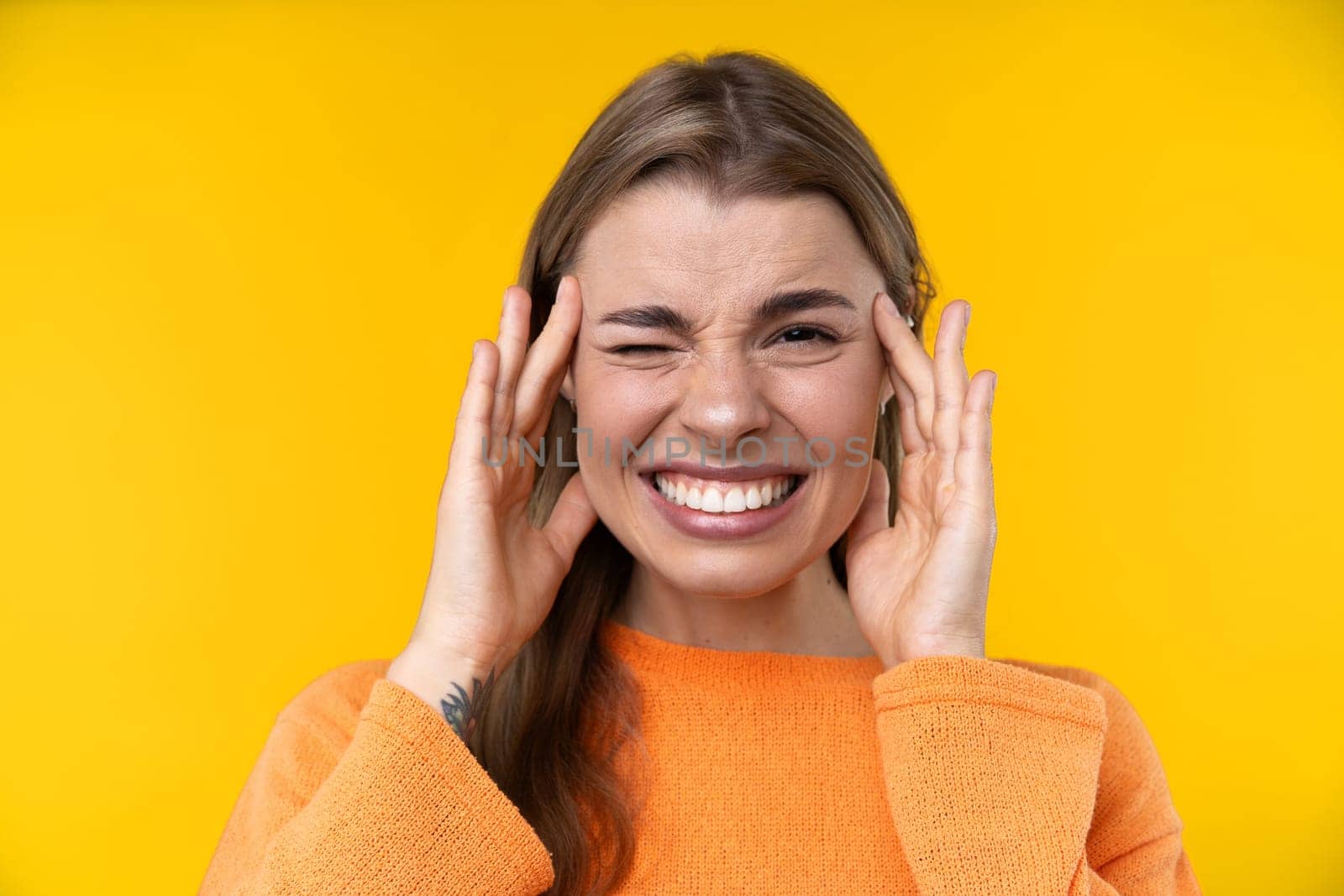 Happy emotions concept. Positive and beautiful young woman laughs poisitively looks aside with carefree face expression wears casual orange sweater isolated over yellow studio background.