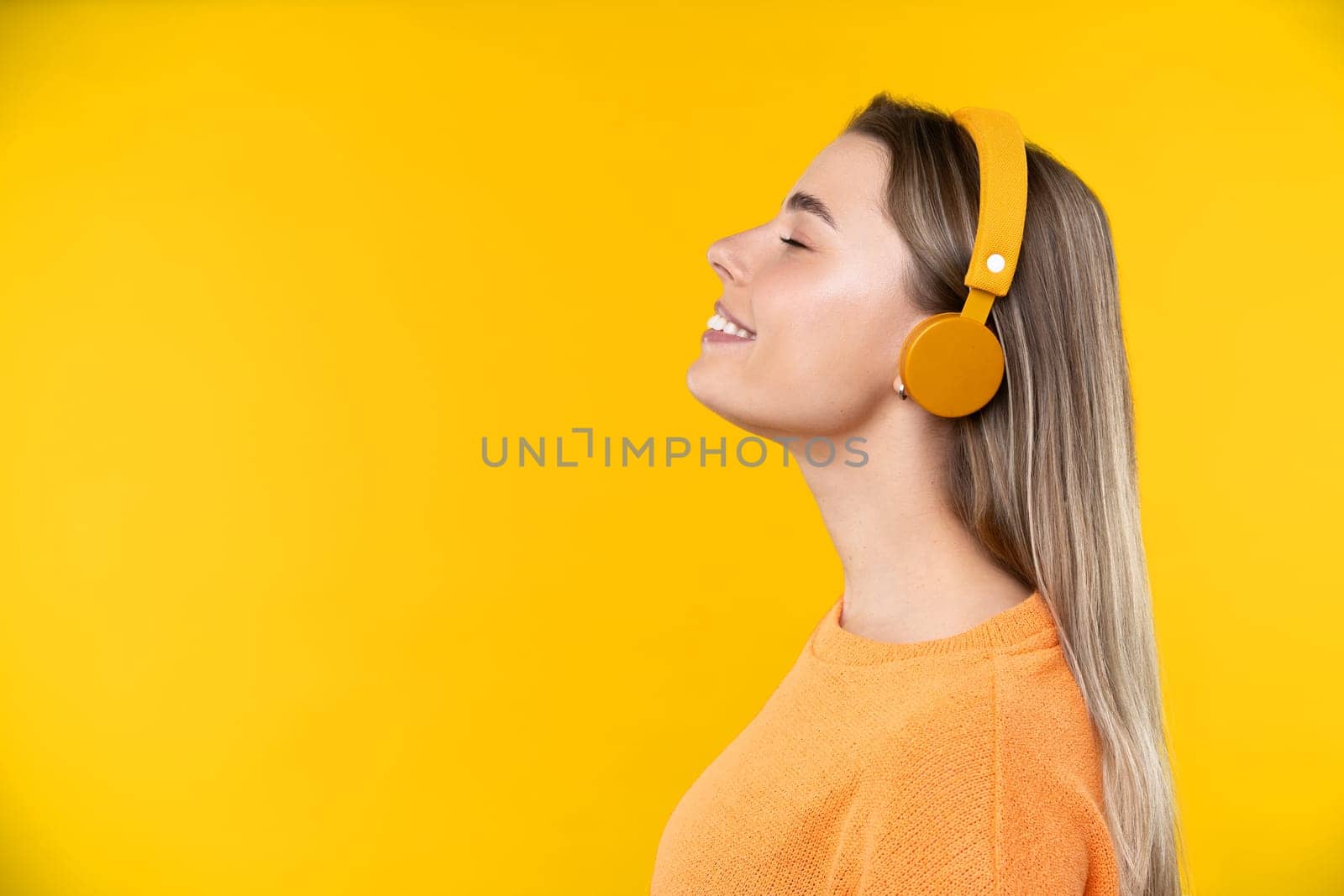 Happy emotions concept. Positive and beautiful young woman laughs poisitively looks aside with carefree face expression wears casual orange sweater isolated over yellow studio background.