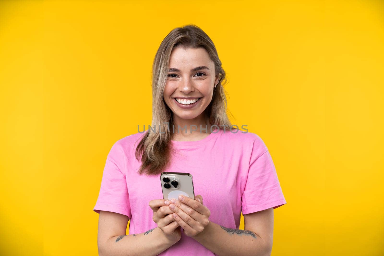 Happy emotions concept. Positive and beautiful young woman laughs poisitively looks aside with carefree face expression wears casual orange sweater isolated over yellow studio background.