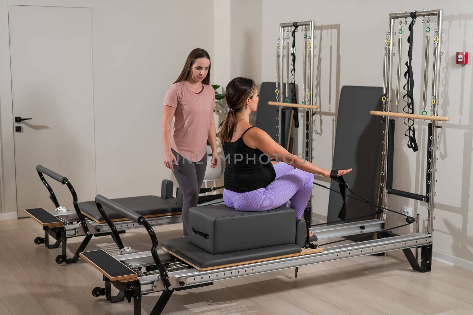 Caucasian pregnant woman doing Pilates exercises on a reformer machine with an individual trainer