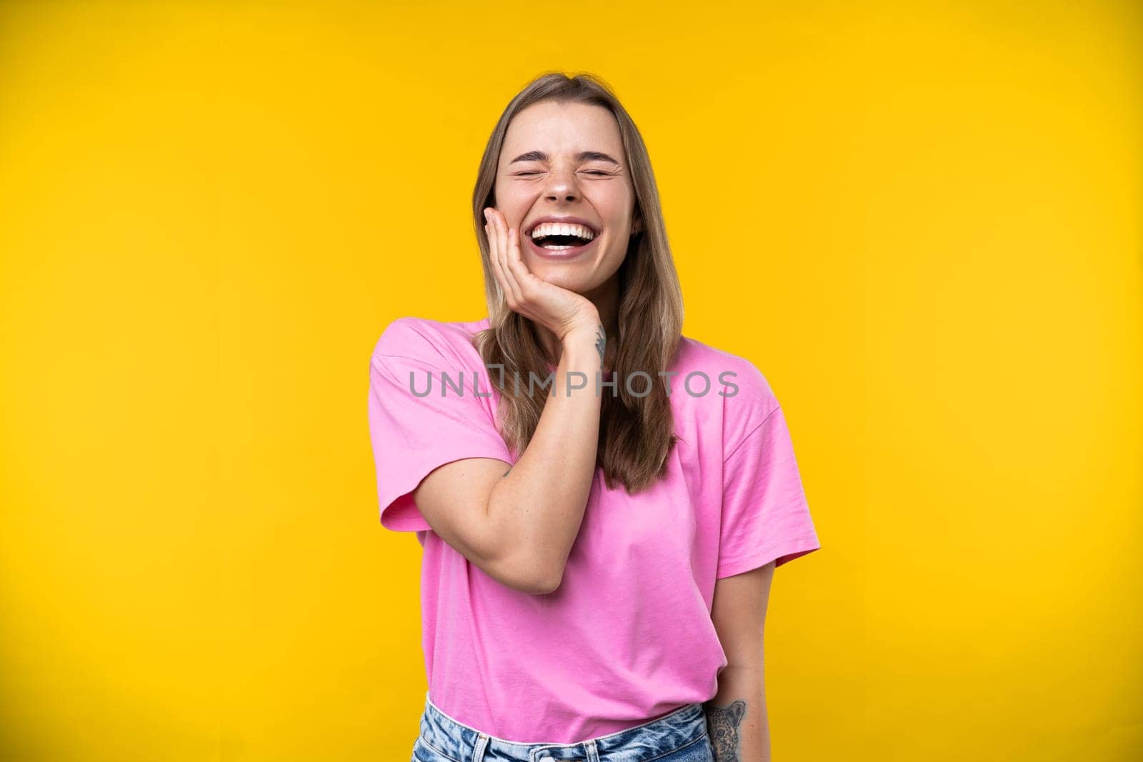 Happy emotions concept. Positive and beautiful young woman laughs poisitively looks aside with carefree face expression wears casual orange sweater isolated over yellow studio background.