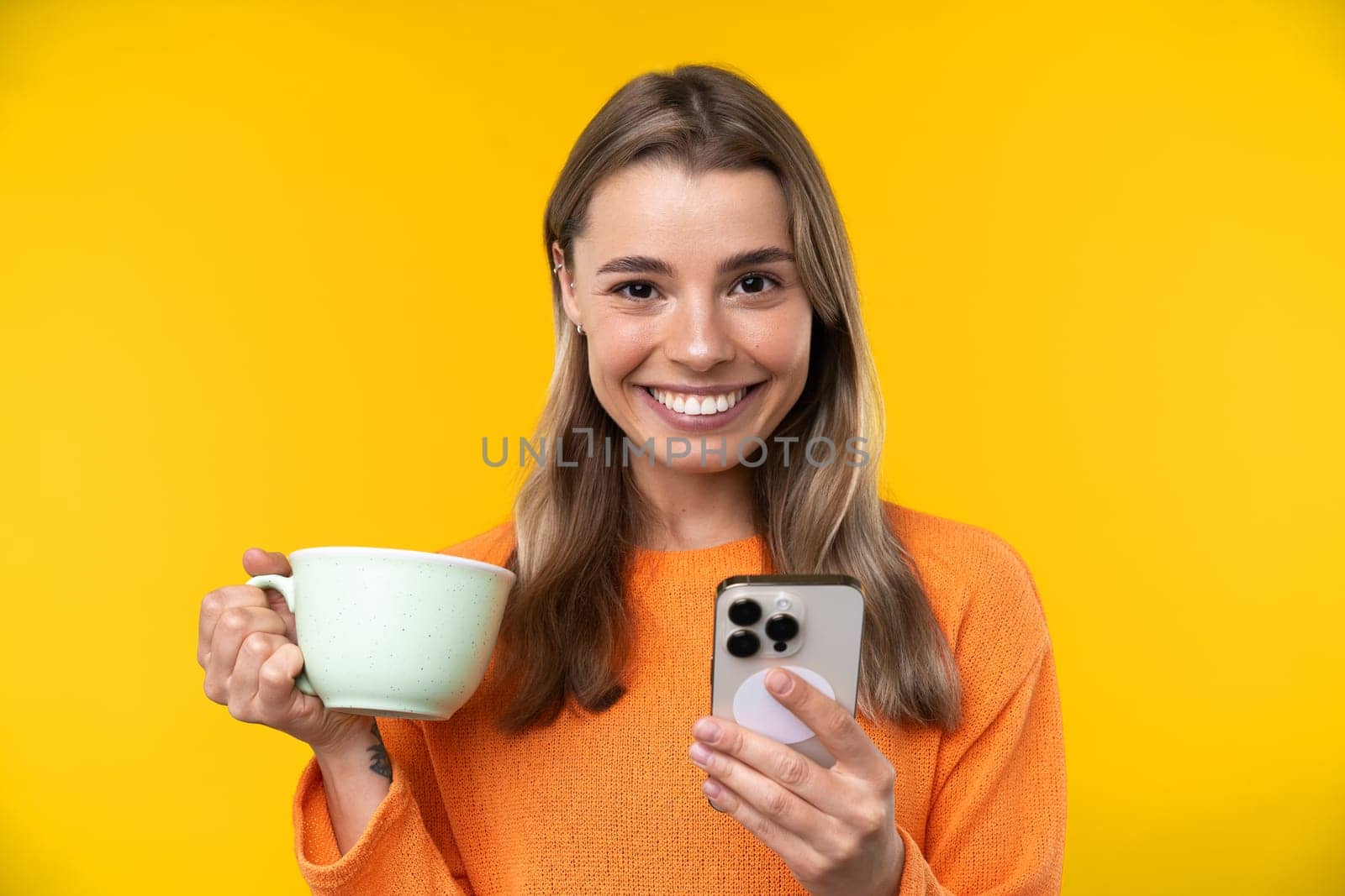 Happy emotions concept. Positive and beautiful young woman laughs poisitively looks aside with carefree face expression wears casual orange sweater isolated over yellow studio background.