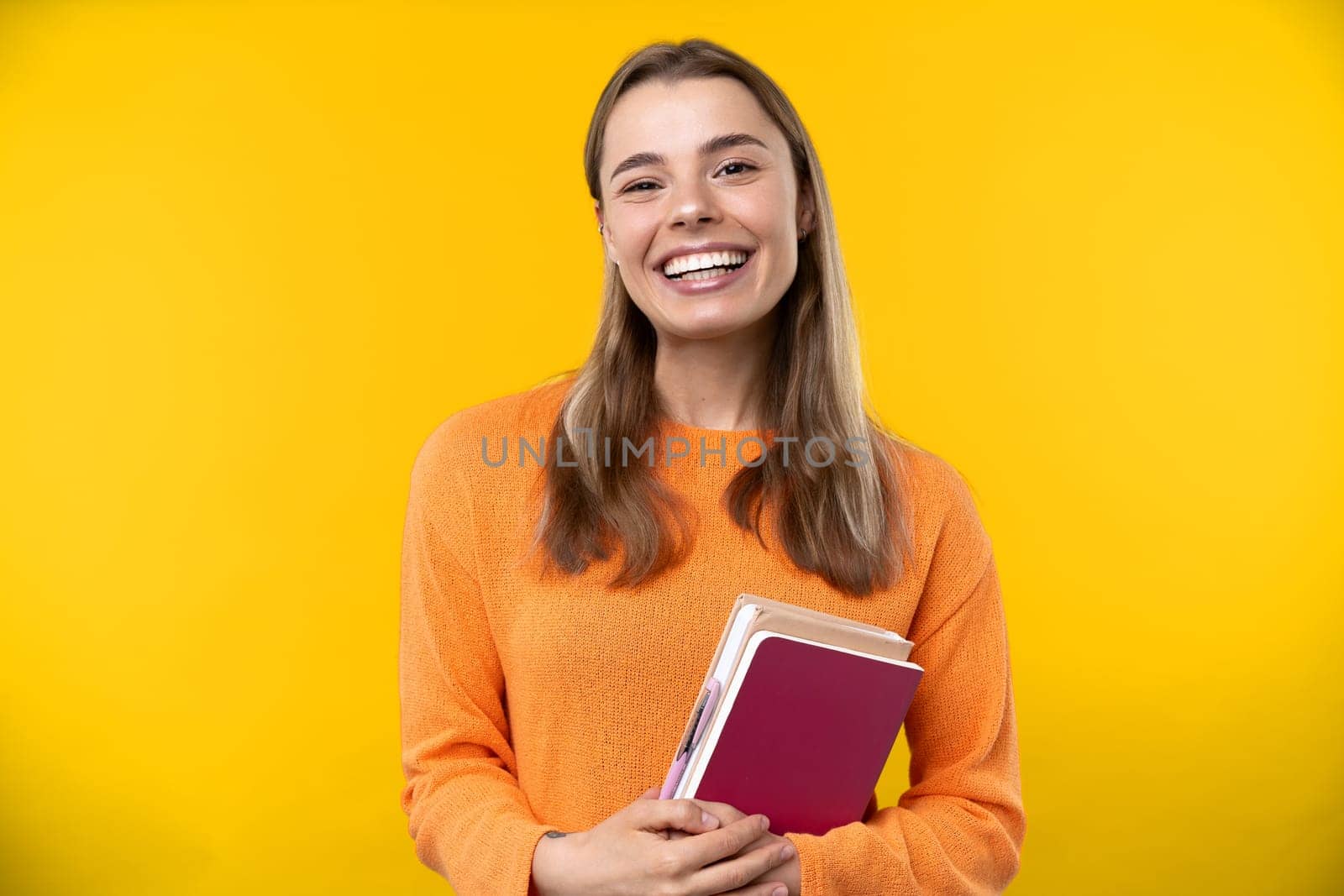 Happy emotions concept. Positive and beautiful young woman laughs poisitively looks aside with carefree face expression wears casual orange sweater isolated over yellow studio background.