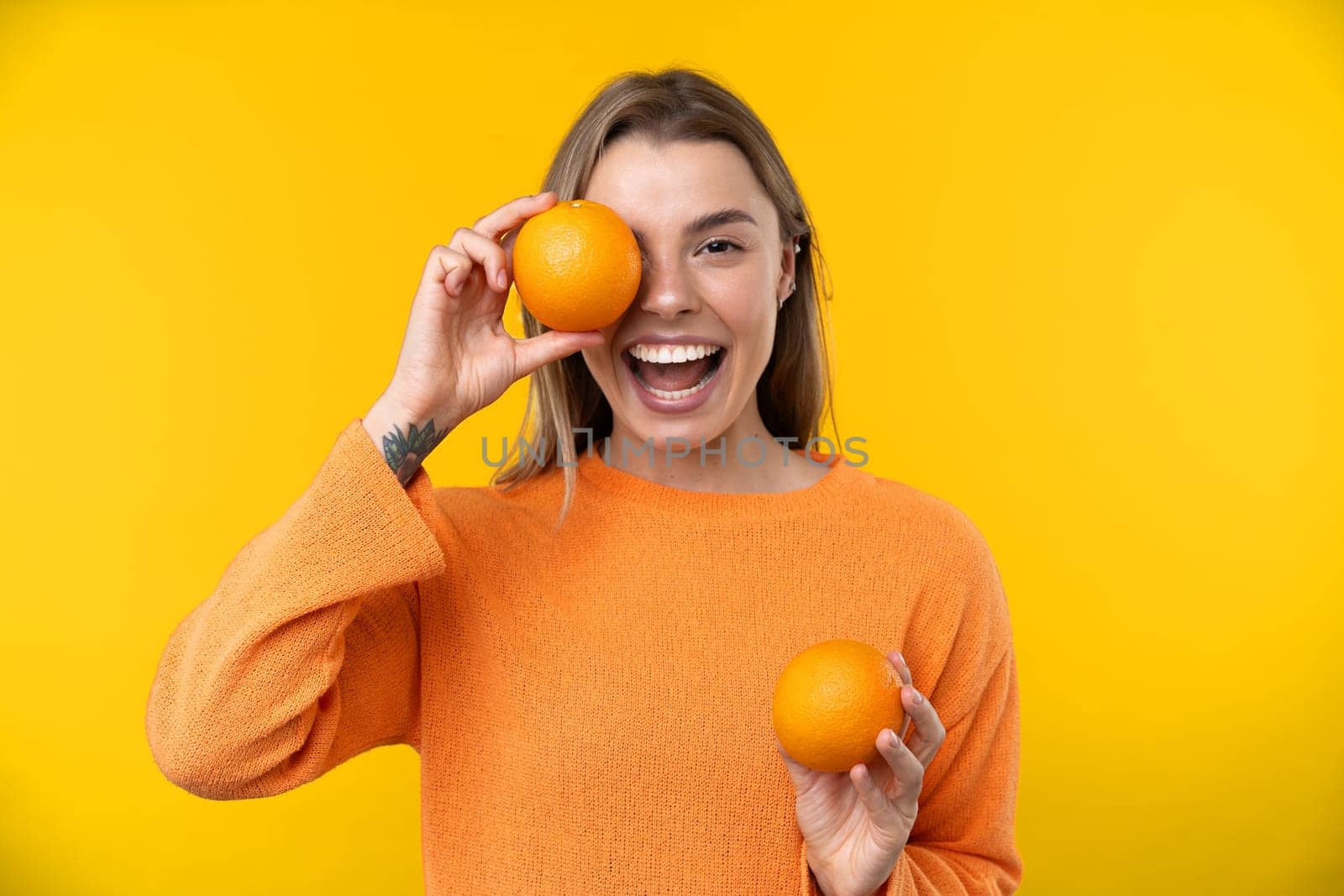 Happy emotions concept. Positive and beautiful young woman laughs poisitively looks aside with carefree face expression wears casual orange sweater isolated over yellow studio background.