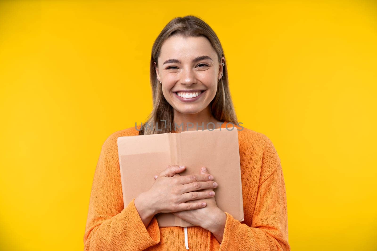 Happy emotions concept. Positive and beautiful young woman laughs poisitively looks aside with carefree face expression wears casual orange sweater isolated over yellow studio background.