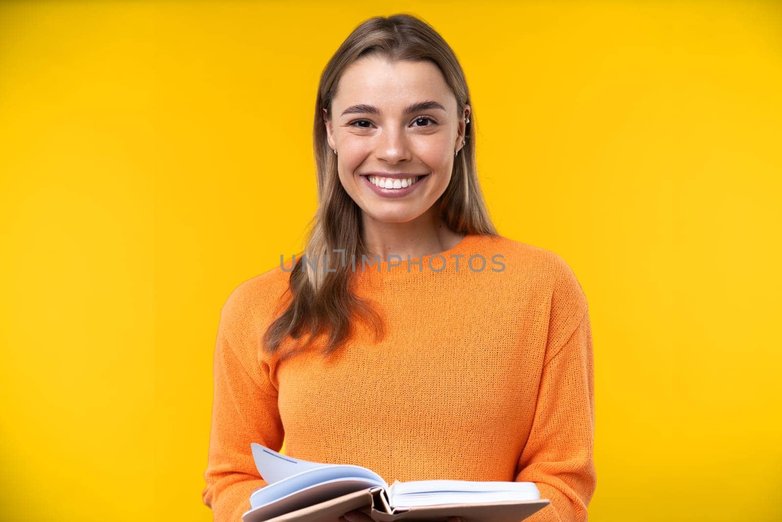 Happy emotions concept. Positive and beautiful young woman laughs poisitively looks aside with carefree face expression wears casual orange sweater isolated over yellow studio background.