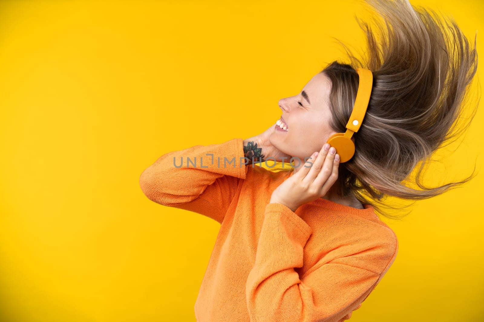 Happy emotions concept. Positive and beautiful young woman laughs poisitively looks aside with carefree face expression wears casual orange sweater isolated over yellow studio background.