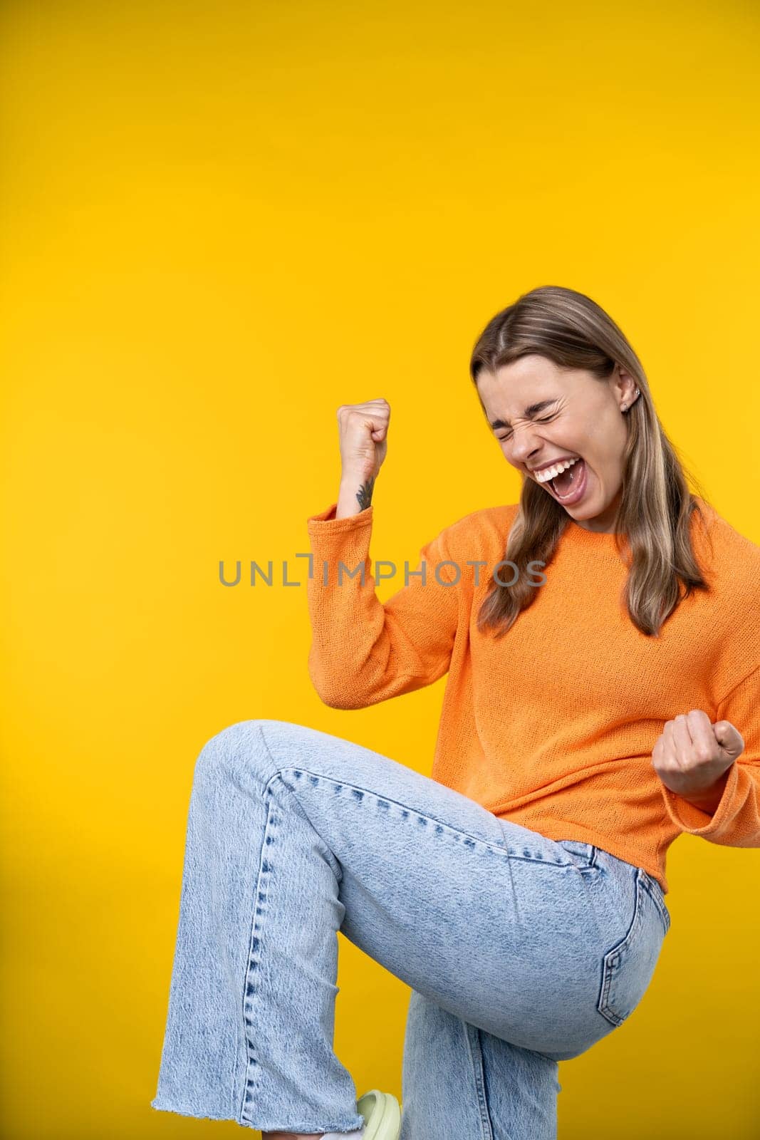 Happy emotions concept. Positive and beautiful young woman laughs poisitively looks aside with carefree face expression wears casual orange sweater isolated over yellow studio background.