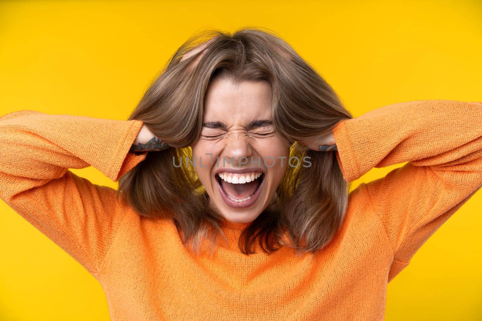 Happy emotions concept. Positive and beautiful young woman laughs poisitively looks aside with carefree face expression wears casual orange sweater isolated over yellow studio background.