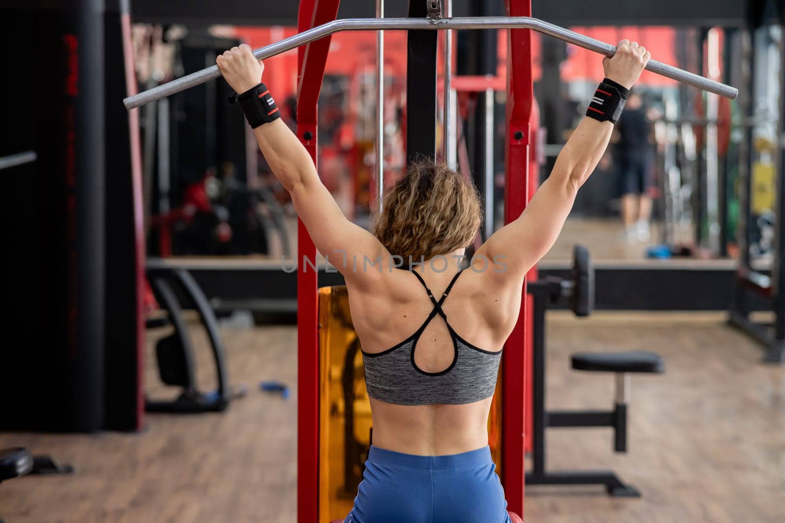 Rear view of a Caucasian forty-year-old woman doing lat pull-downs in the gym