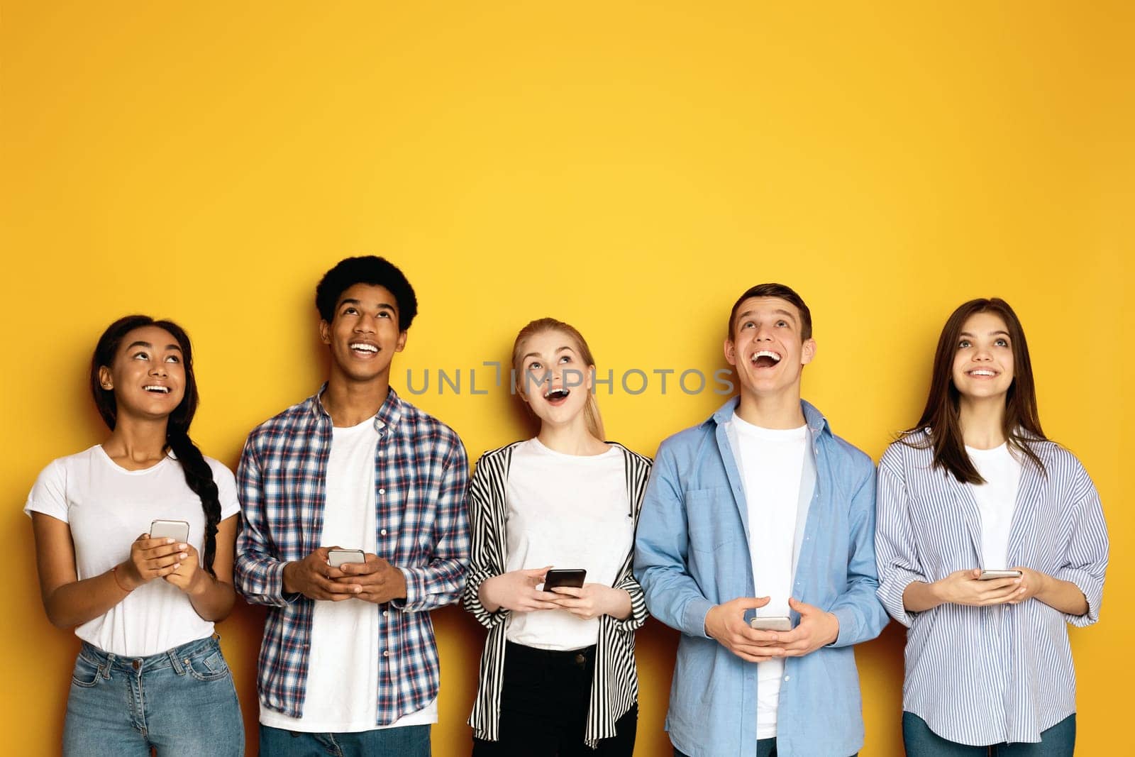 A joyful moment shared among a multiethnic group of teenagers, all looking upwards and laughing with genuine happiness.