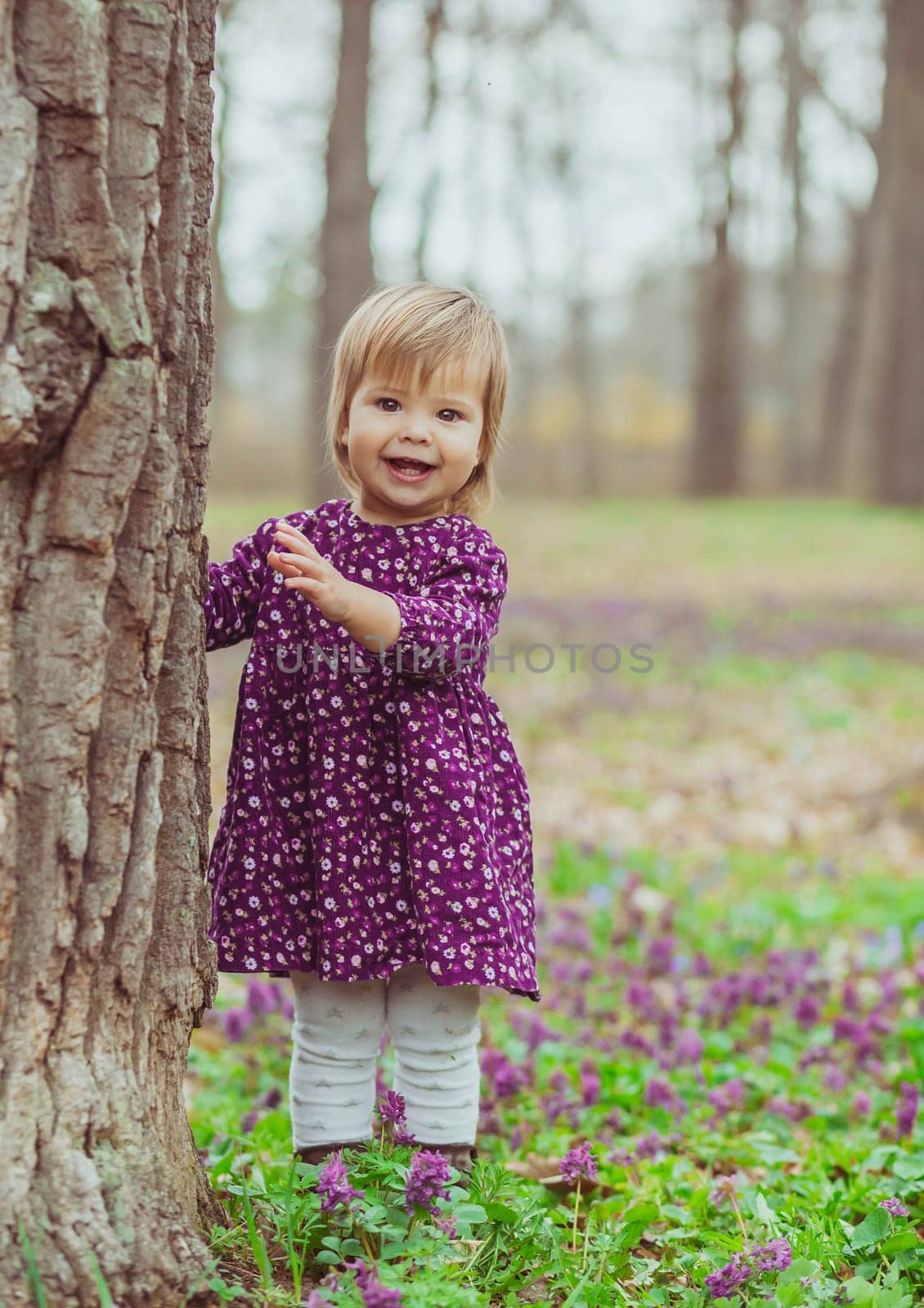 blond baby in a colored dress running in a forest glade with flowers.