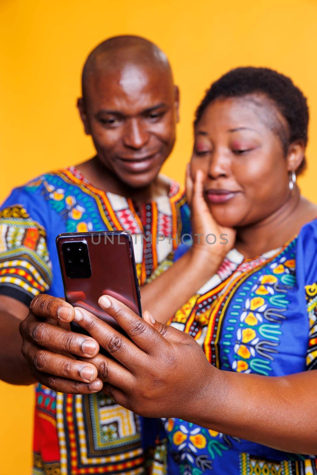 African american couple wearing ethnic clothes taking selfie on smartphone. Man and woman in relationship making photo together while holding mobile phone in hand closeup