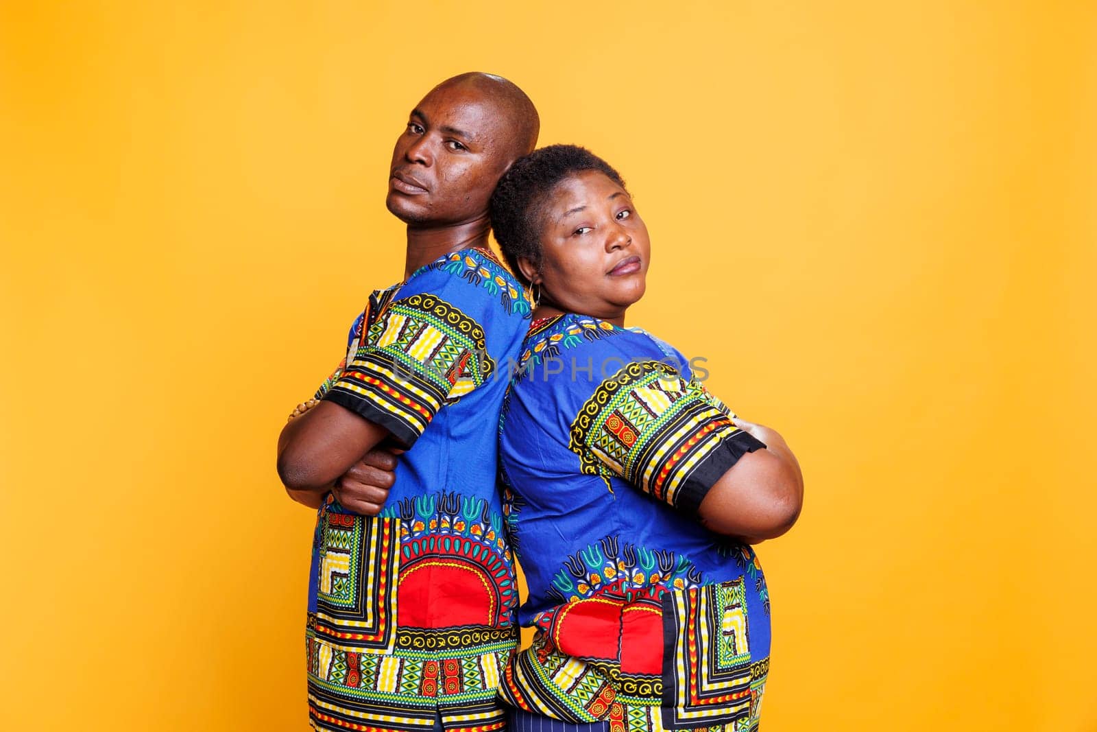 Confident man and woman with folded hands standing back to back and looking at camera. African american couple wearing ethnic clothes posing with arms crossed studio portrait