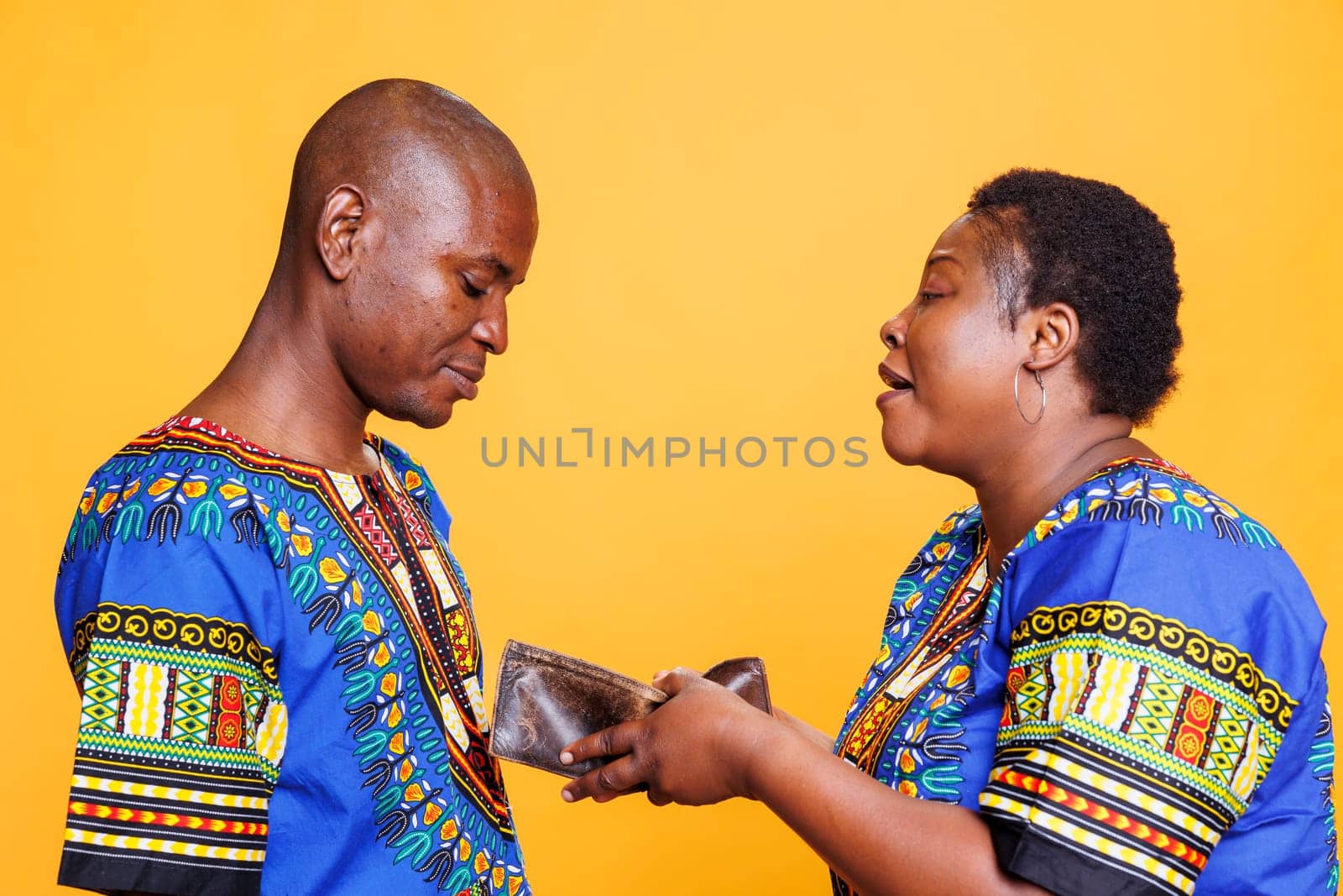 Woman holding open empty wallet with no finance and shouting at unhappy husband. African american couple having conflict while discussing financial problem and displaying purse with no money