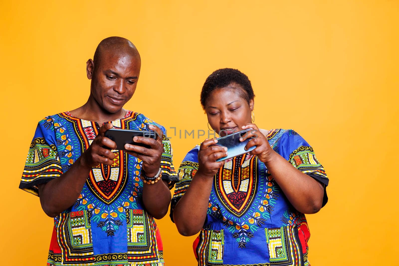 Concentrated black man and woman couple enjoying mobile game on phones and having competition. African american wife and husband gamers pair playing videogame using smartphone app