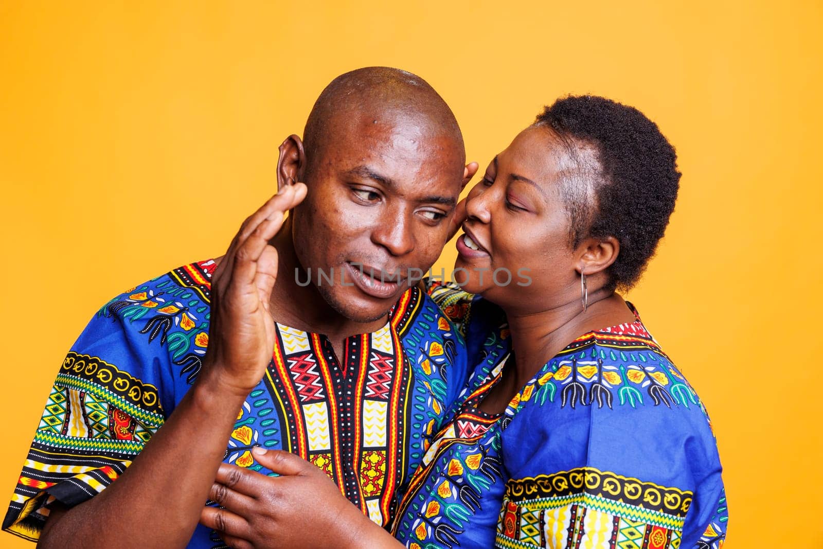 African american man listening to wife whispering with smile on face. Cheerful mid adult woman telling secret to boyfriend in ear, showing relationship bonding and love concept