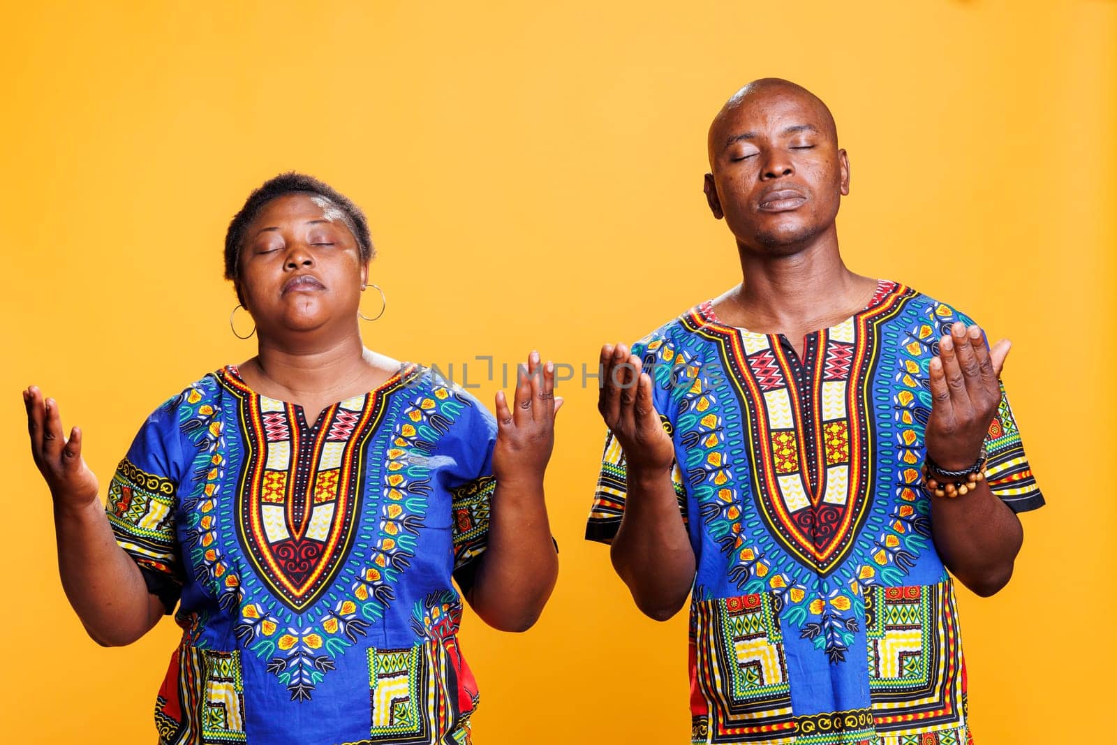 African american couple praying and asking blessing while posing with arms wide open. Religious man and woman prayers pair with closed eyes spreading hands and pleading god