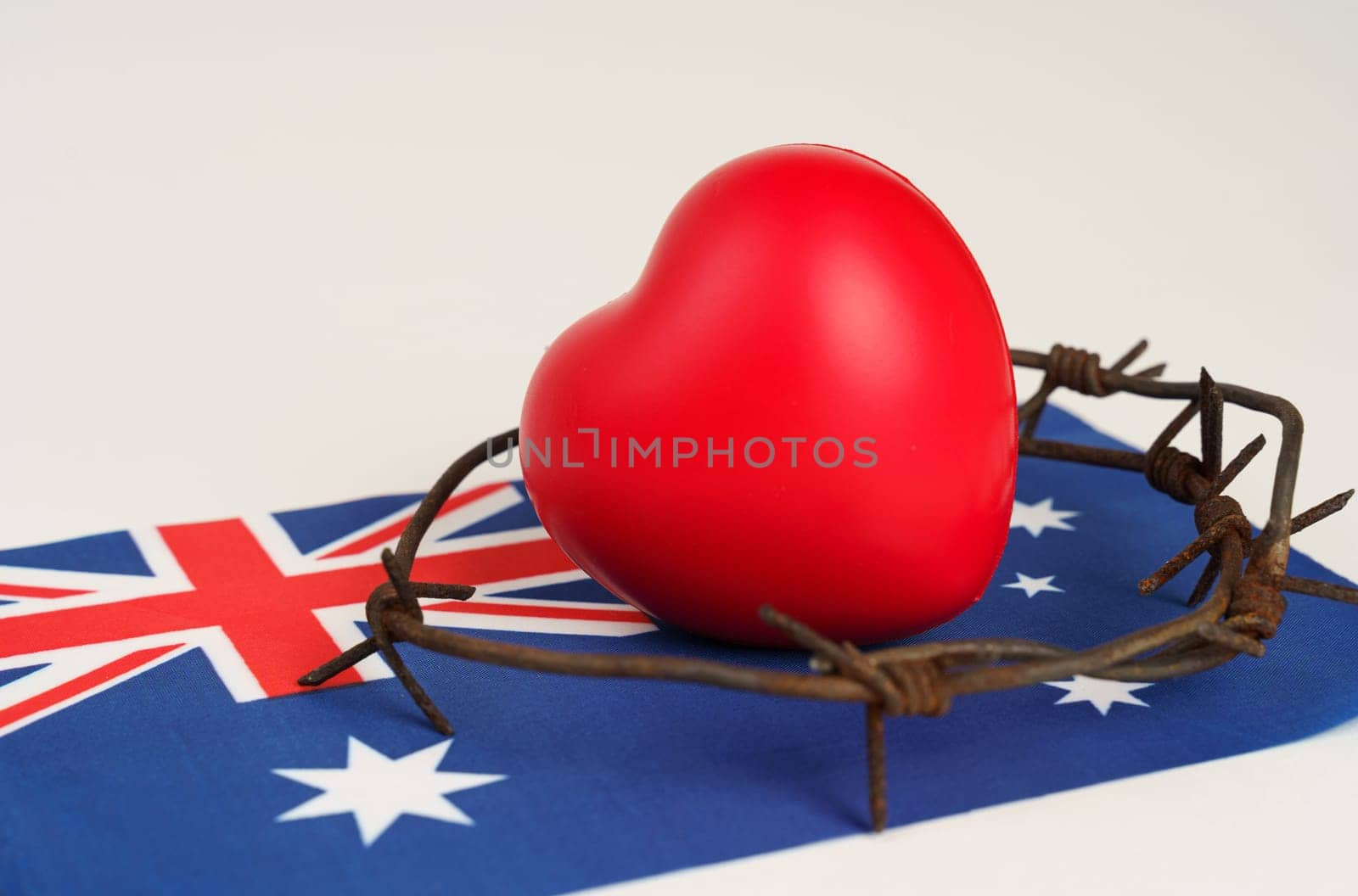 A vibrant red heart wrapped in barbed wire sits atop an Australian flag, depicting a struggle for love and freedom amidst constraints.