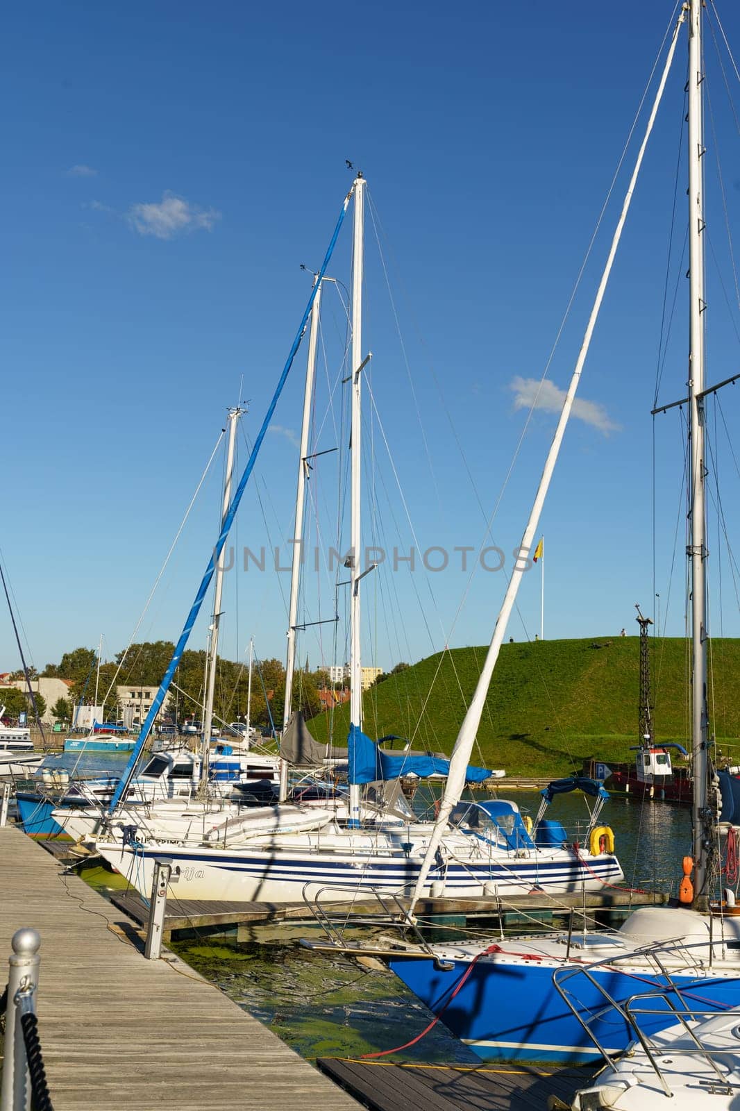 Klaipeda, Lithuania - August 11, 2023: A group of sailboats are secured to a pier, their masts reaching towards the sky as they rest on calm waters.