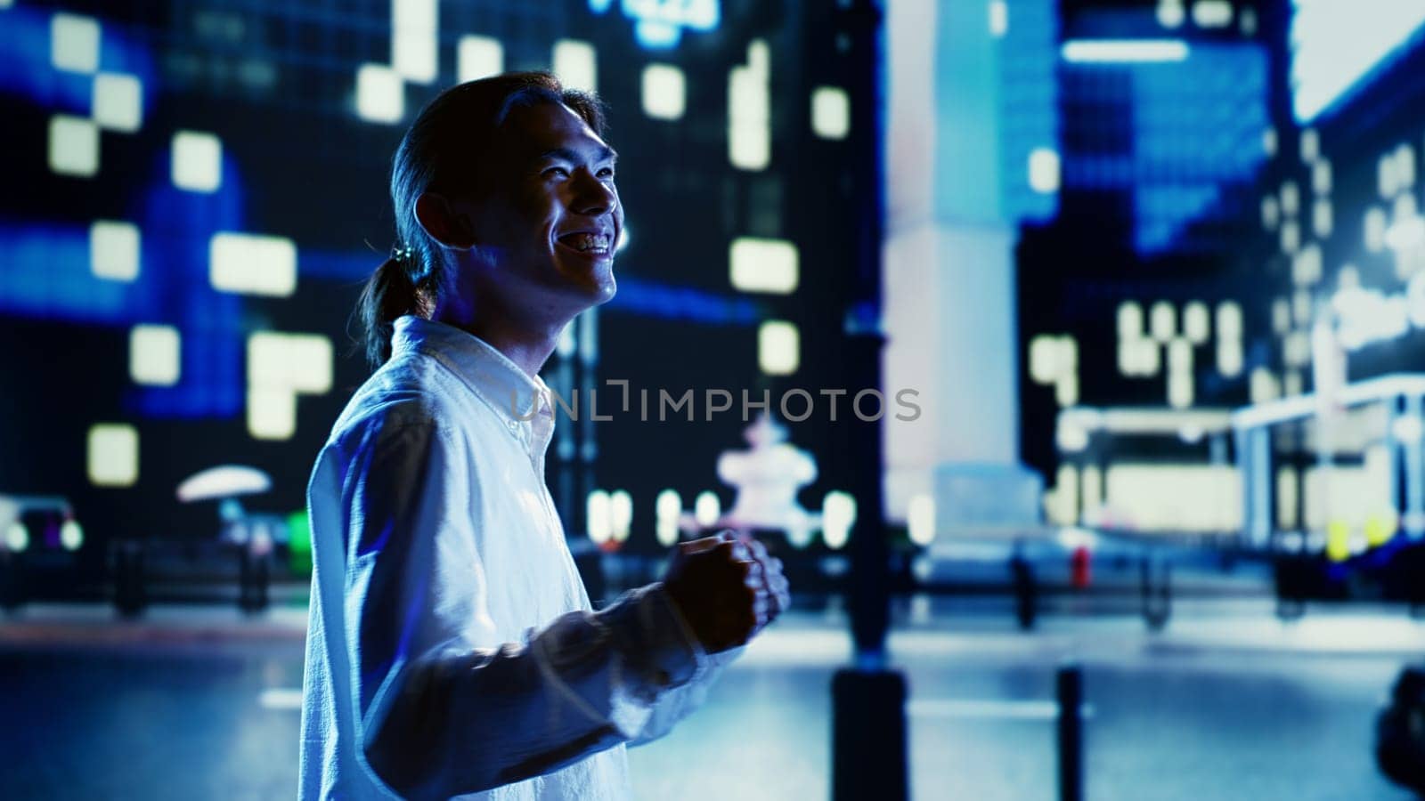 Asian man wandering around city streets at night, laughing and feeling grateful in empty urban environment with no vehicles. Elated businessman taking a walk to celebrate career advancement